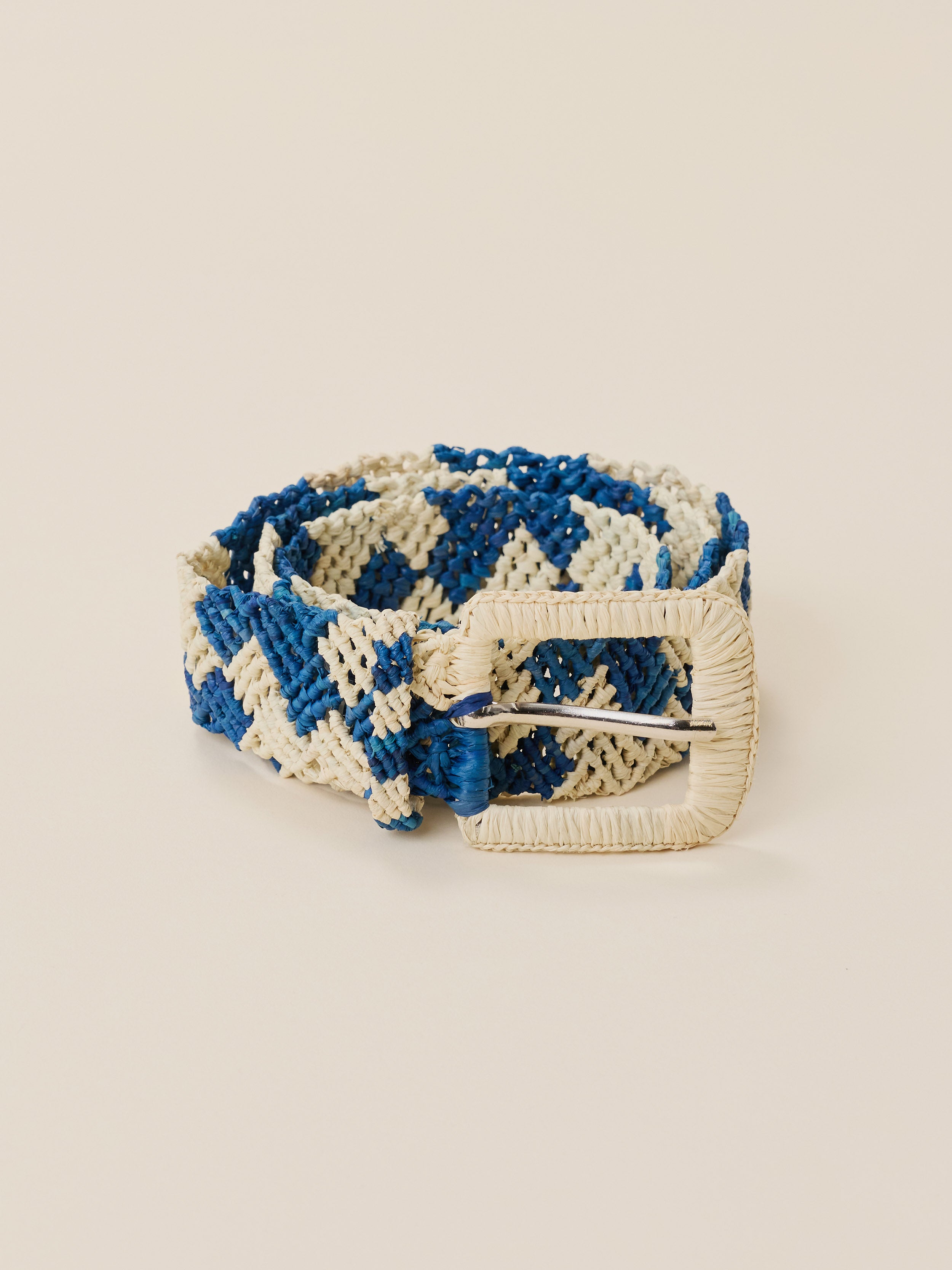 A woven belt with a blue and cream geometric pattern and a cream-colored buckle, displayed on a solid beige background.