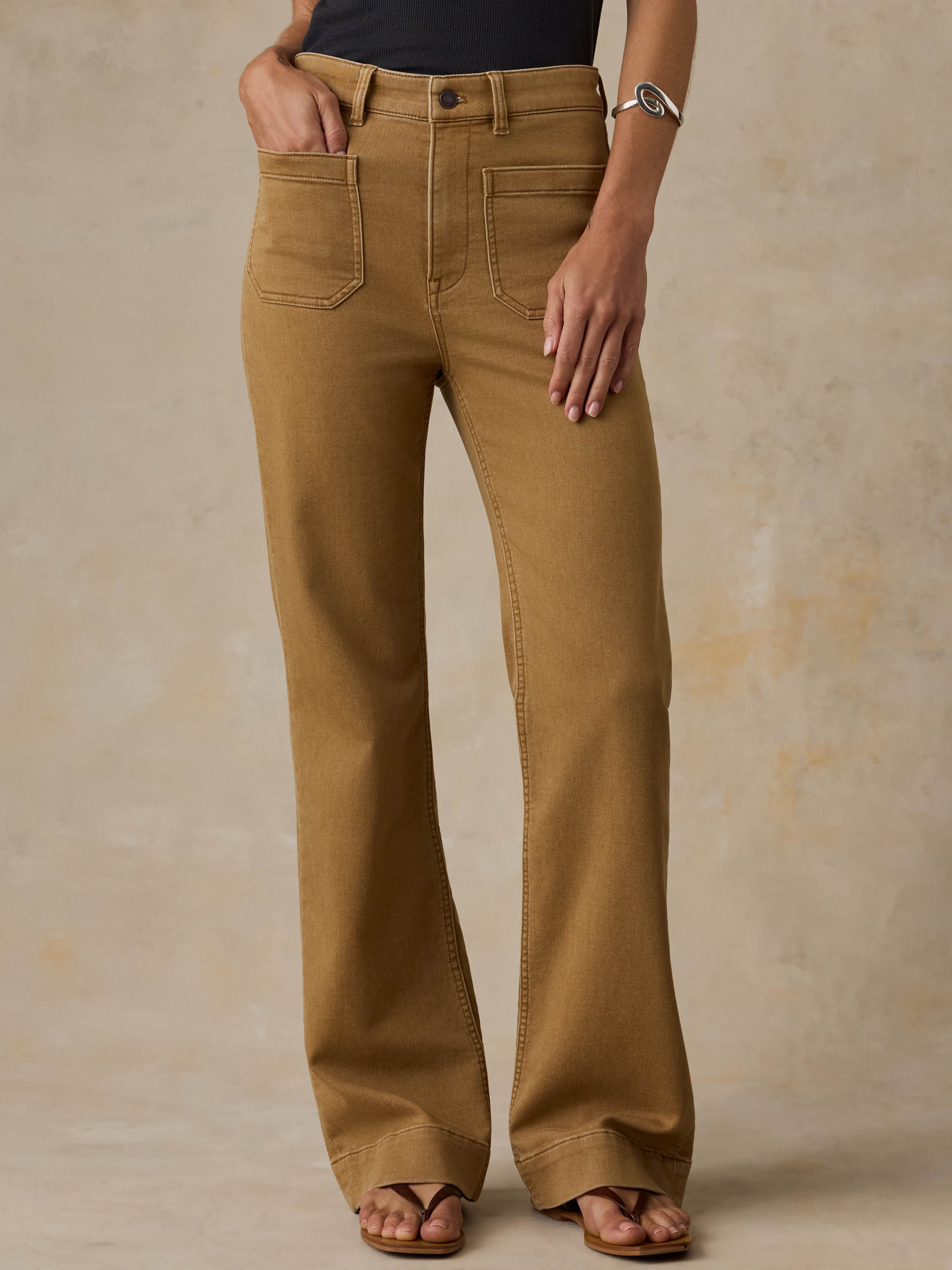 Woman wearing a black tank top and brown pants against a beige background