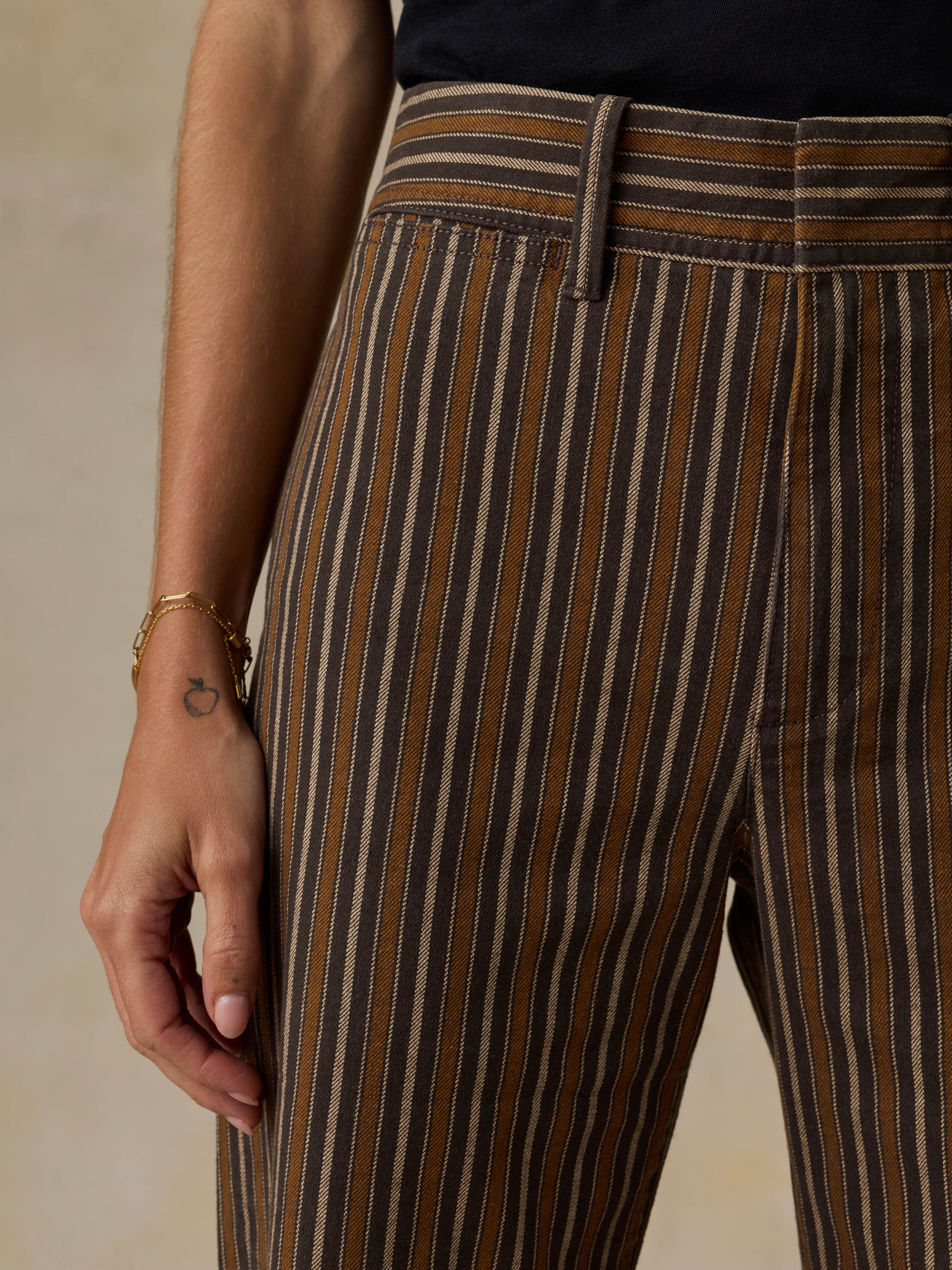 Woman wearing a black t-shirt and brown striped pants on a beige background