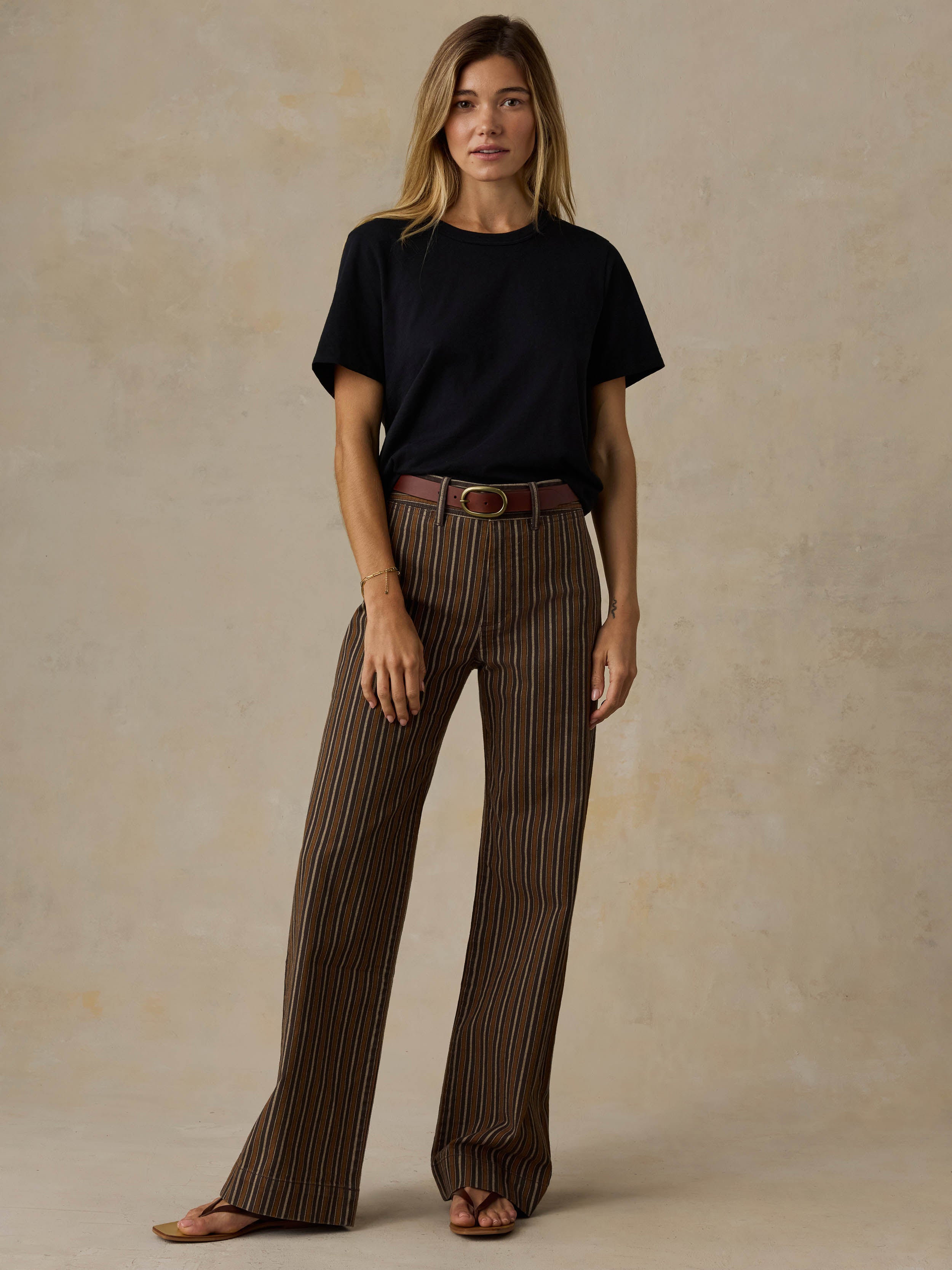 Woman wearing a black t-shirt and brown striped pants on a beige background