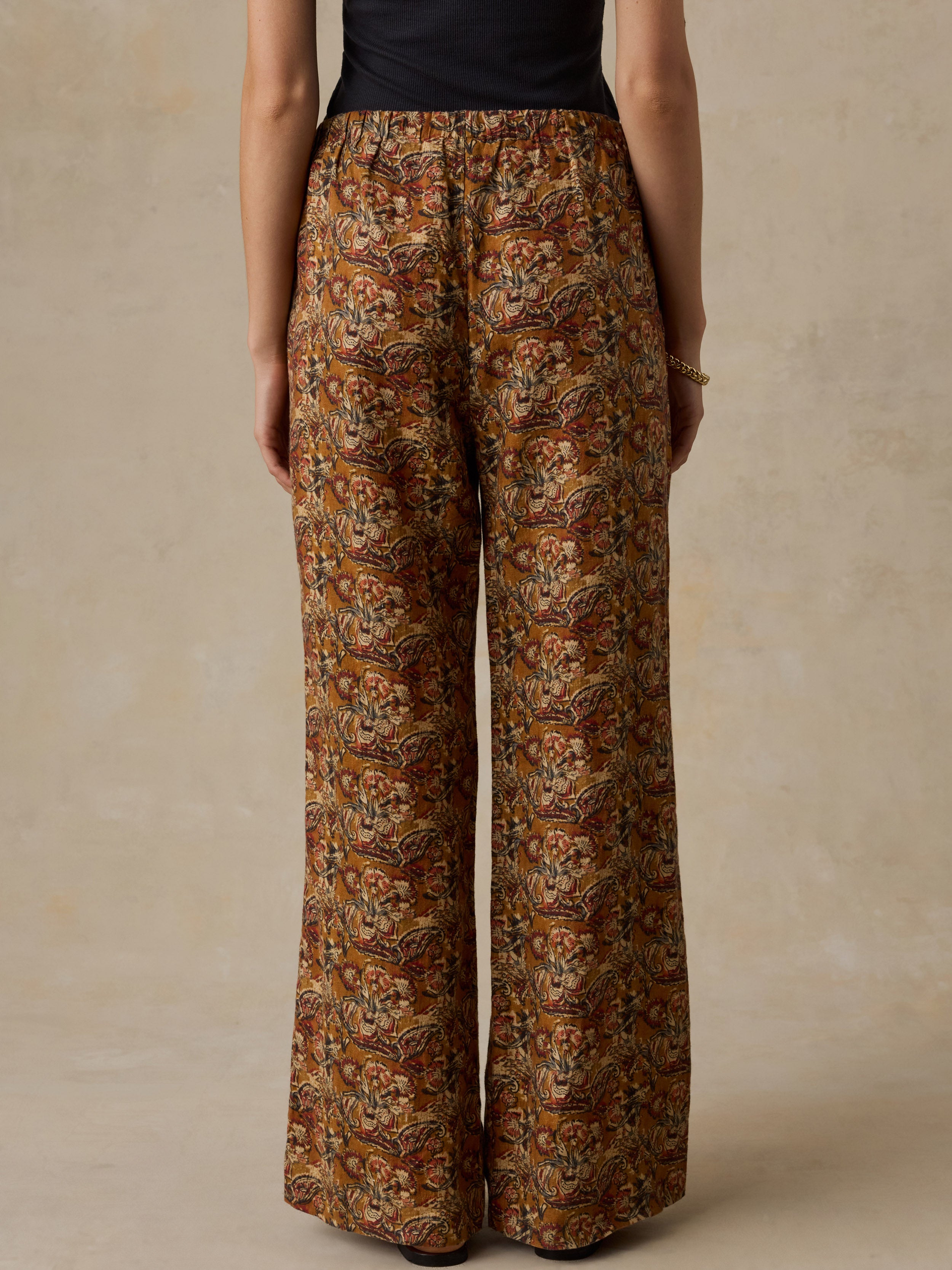Woman wearing a black top with orange floral printed pants against a beige background