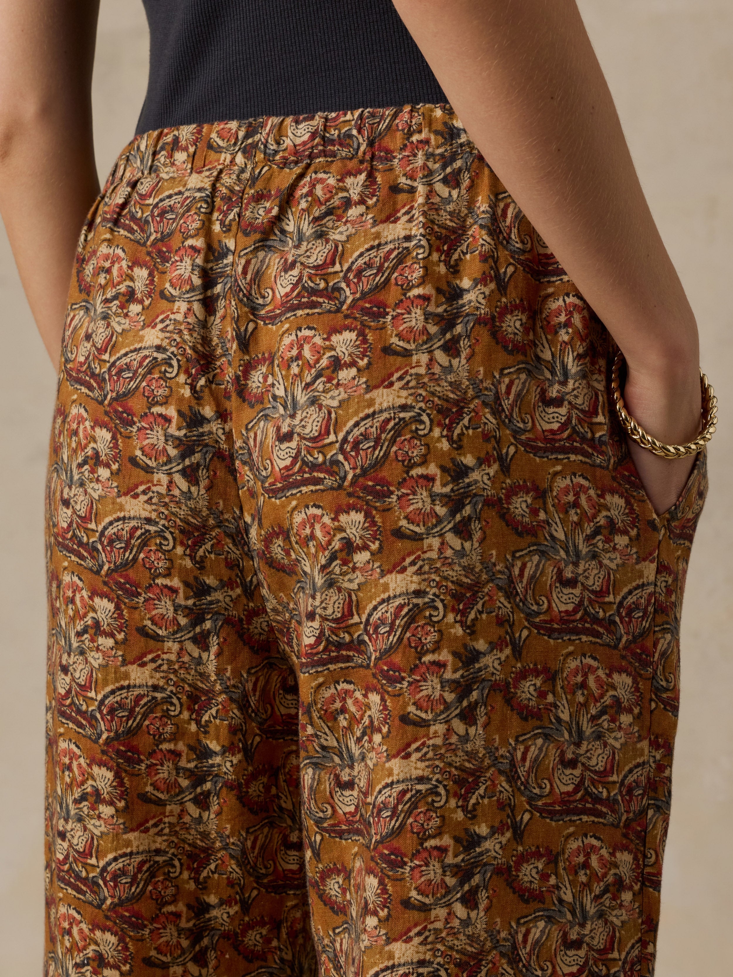 Woman wearing a black top with orange floral printed pants against a beige background