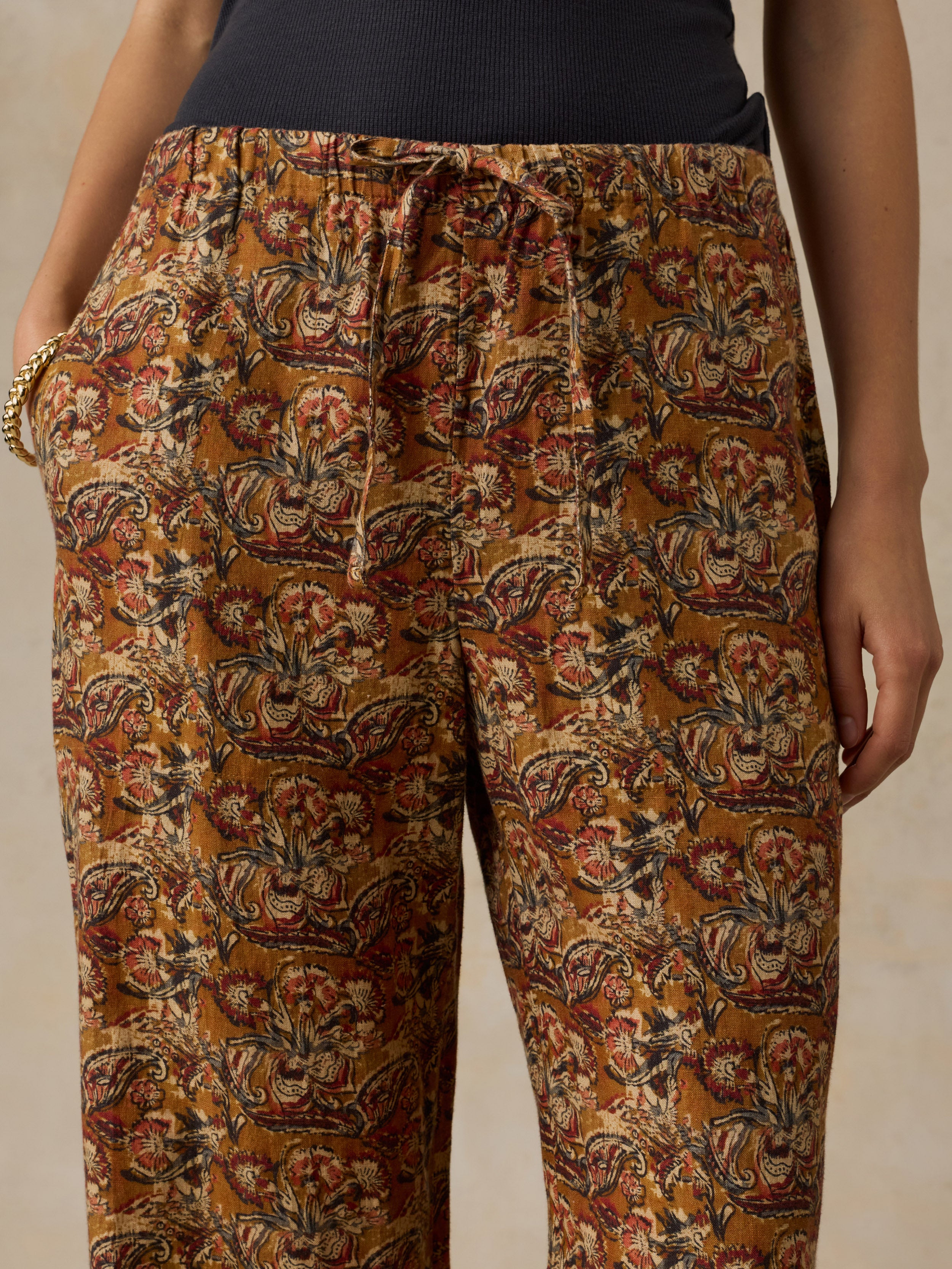 Woman wearing a black top with orange floral printed pants against a beige background