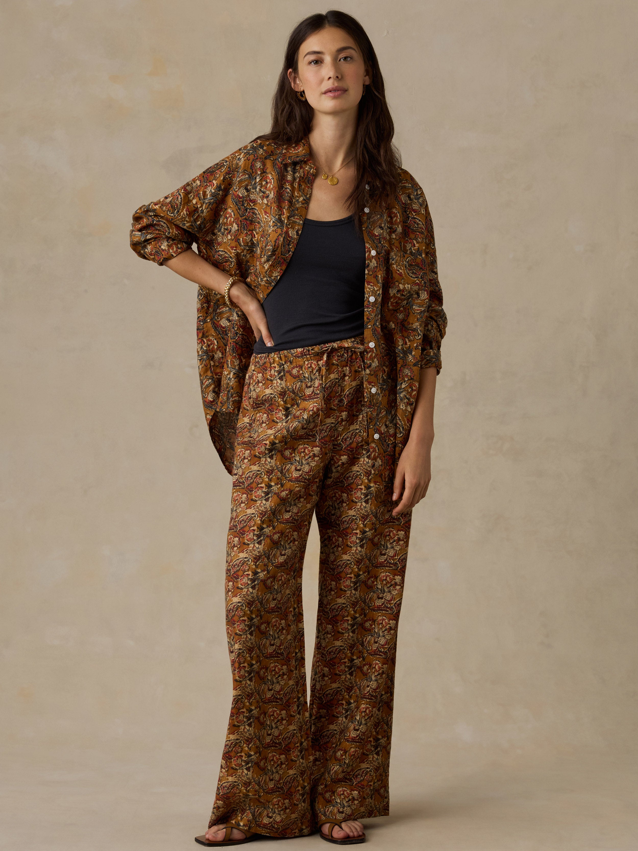 Woman wearing an orange floral printed button up shirt and matching pants against a beige background