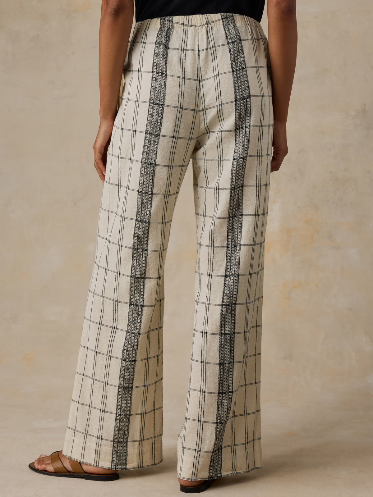 Woman wearing a black t-shirt and white and black plaid pants against a beige background, image 3 of 6