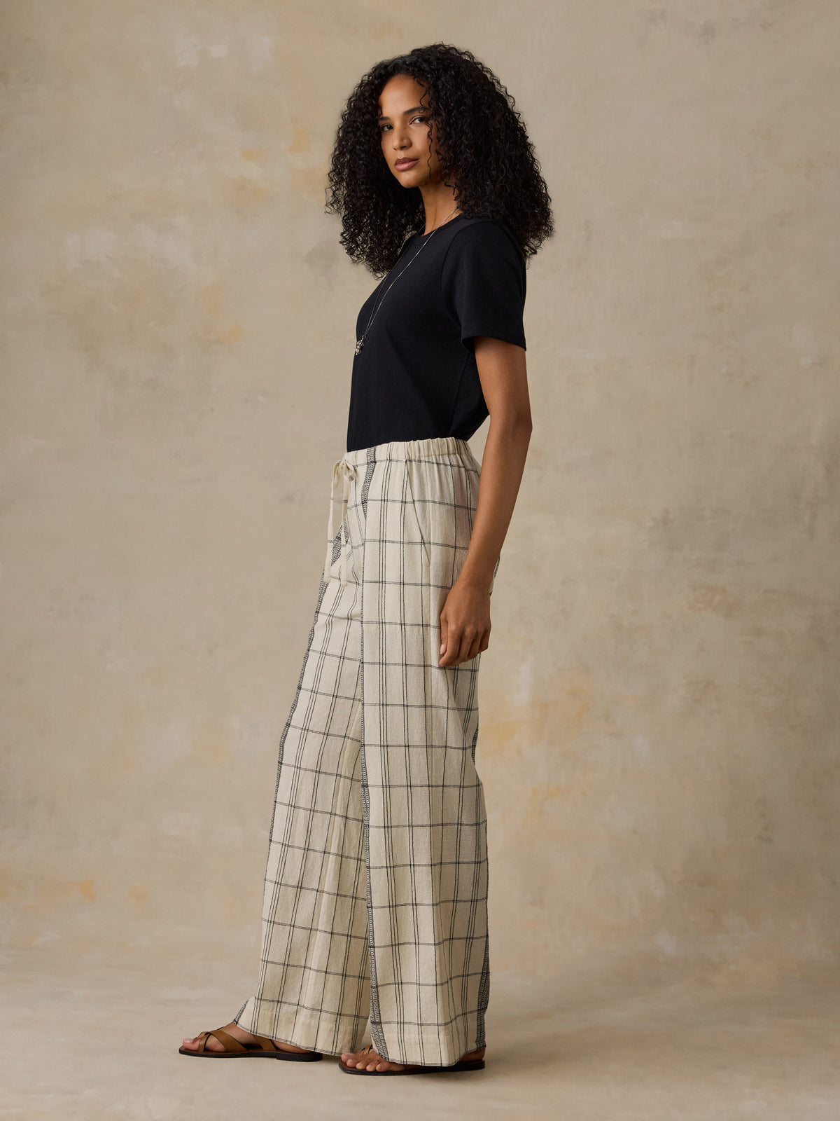 Woman wearing a black t-shirt and white and black plaid pants against a beige background, image 4 of 6