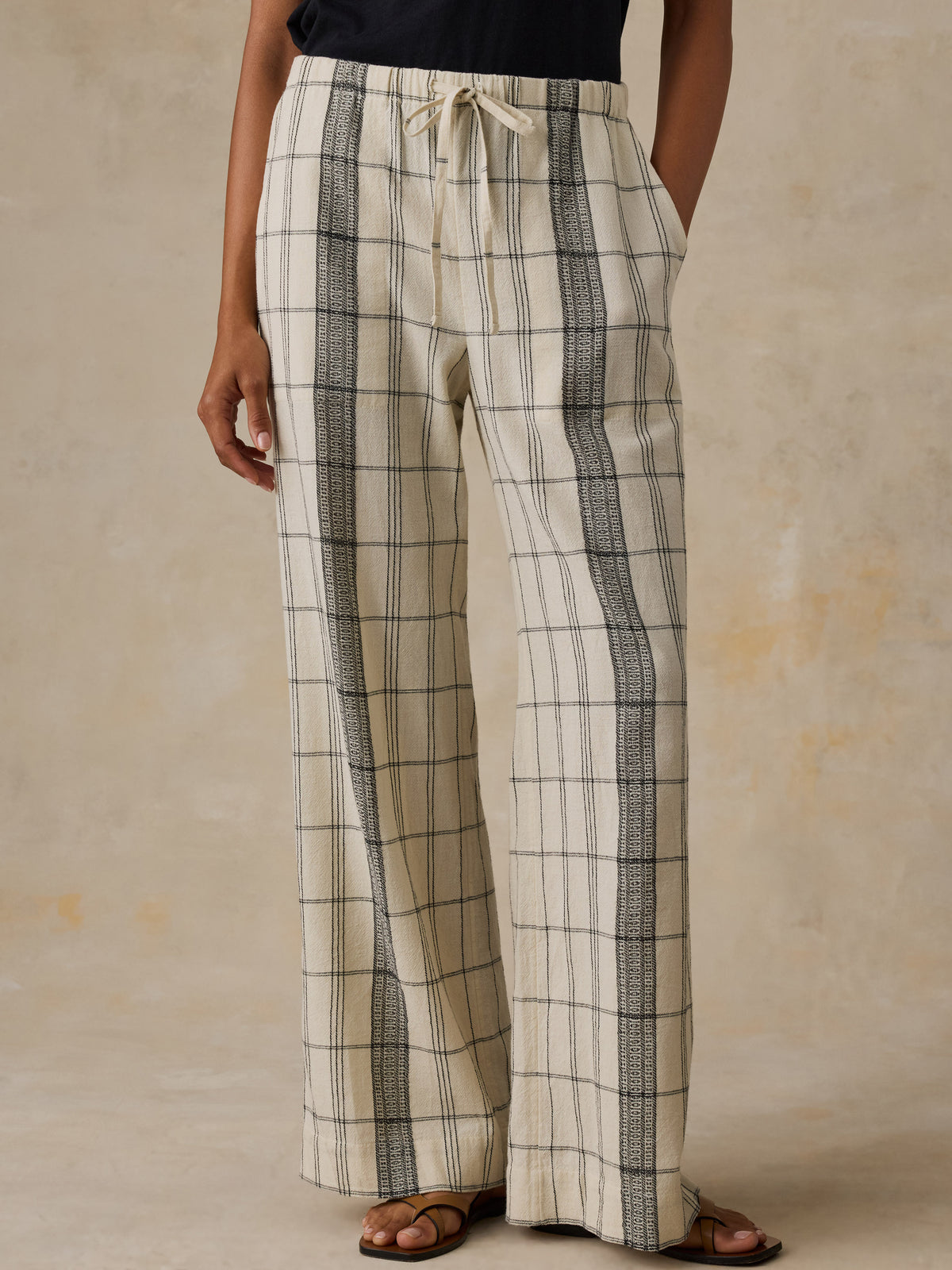 Woman wearing a black t-shirt and white and black plaid pants against a beige background, image 2 of 6