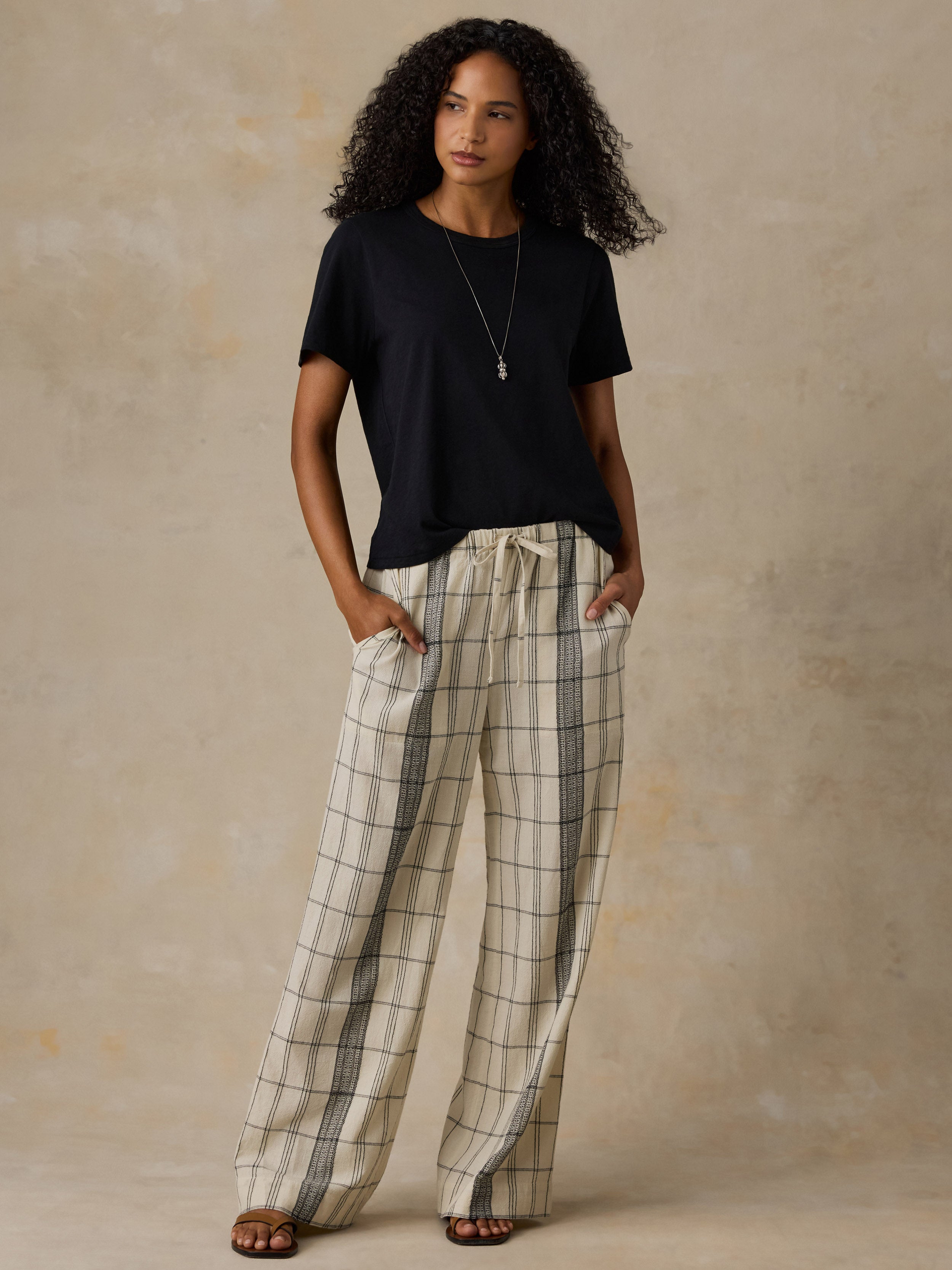 Woman wearing a black t-shirt and white and black plaid pants against a beige background