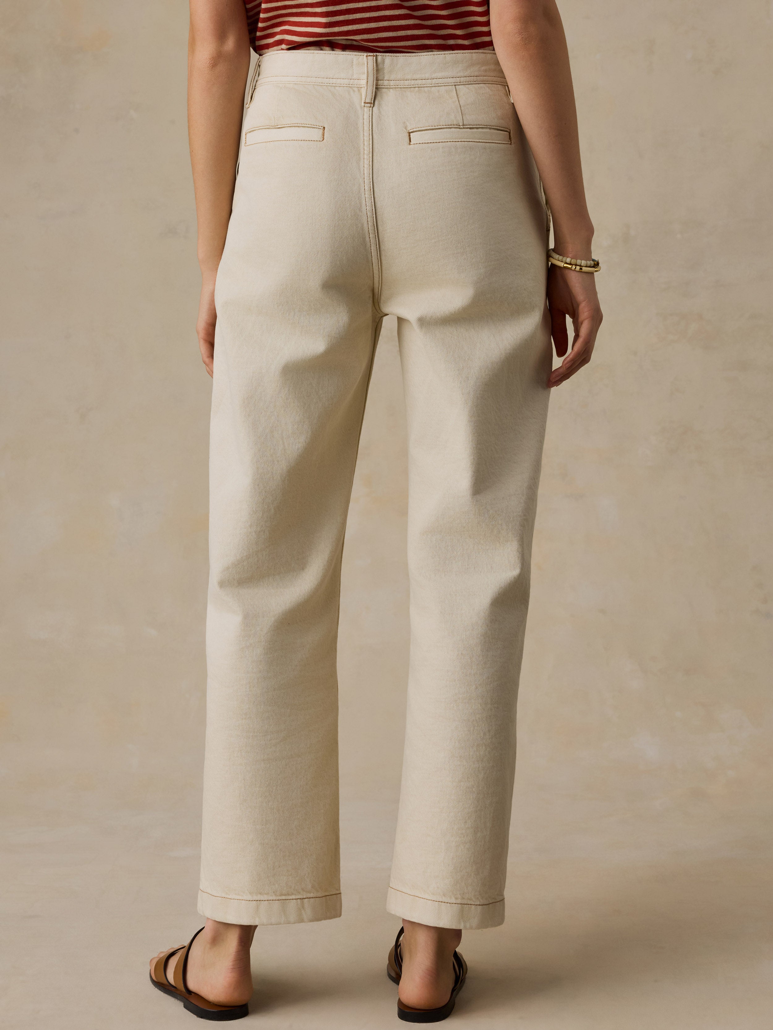 Woman wearing a red and white striped t-shirt and cream colored denim jeans against a beige background