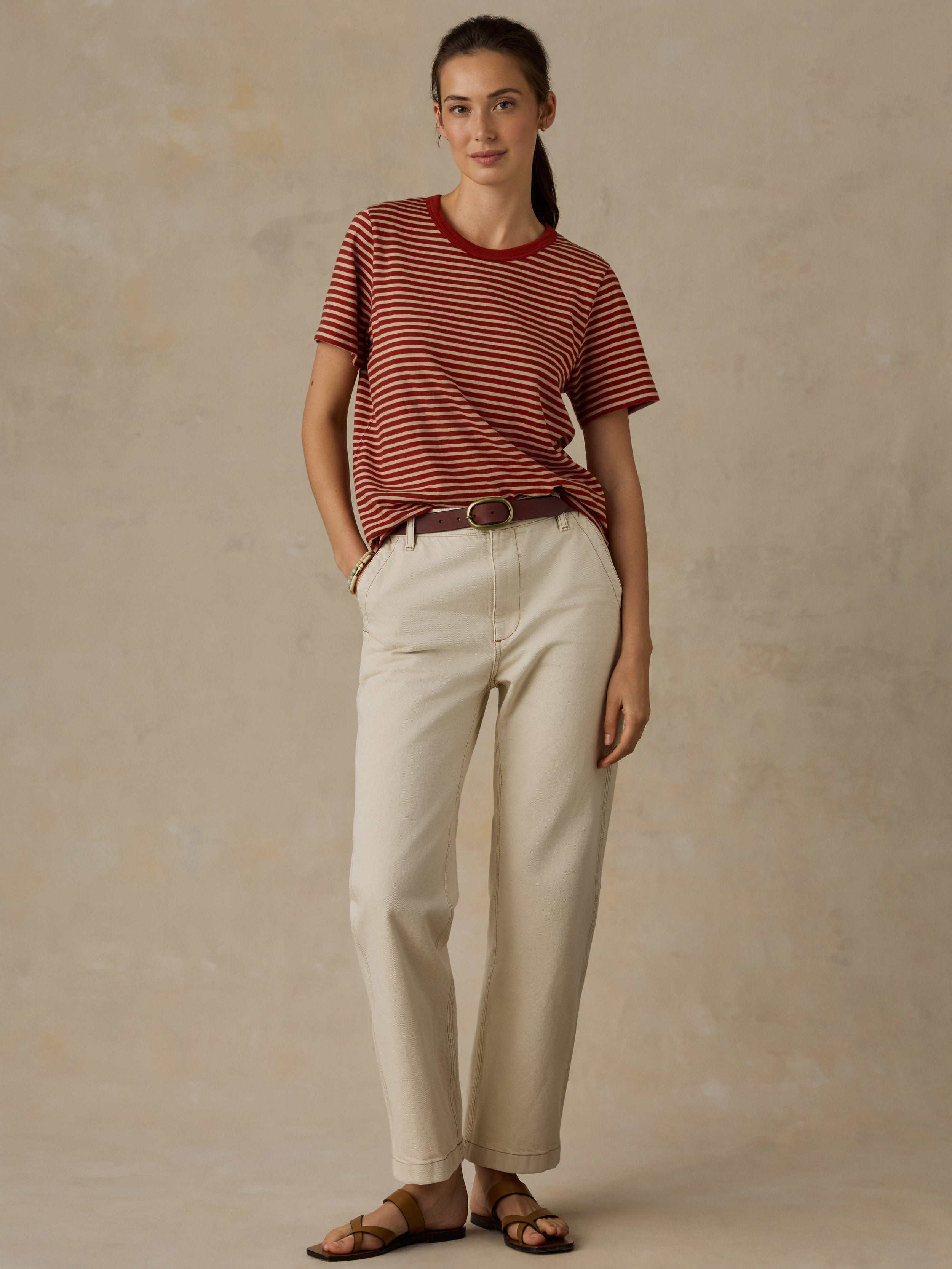 Woman wearing a red and white striped t-shirt and cream colored denim jeans against a beige background