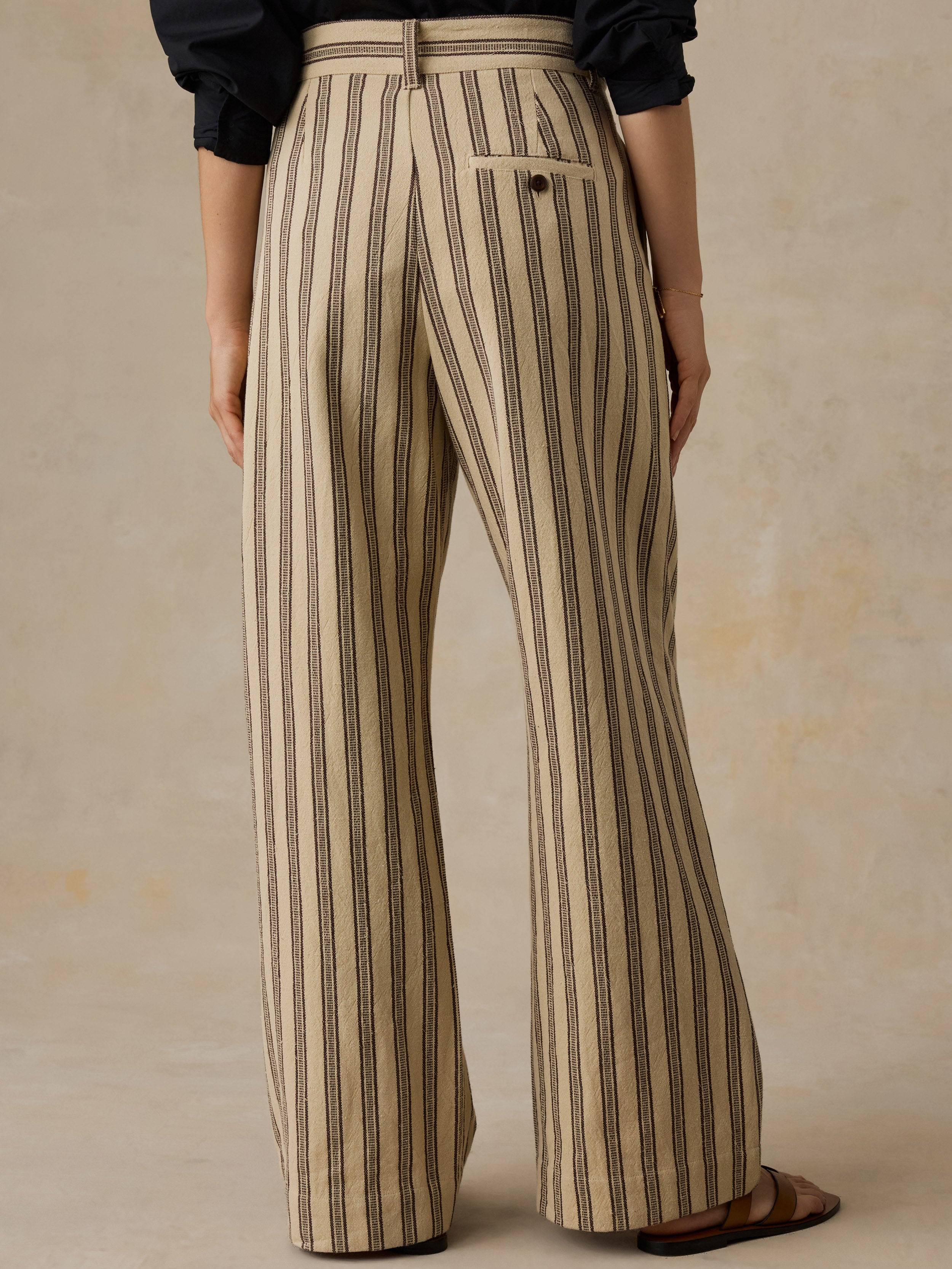 Woman wearing a black button down shirt and beige and black striped pants against a beige background.