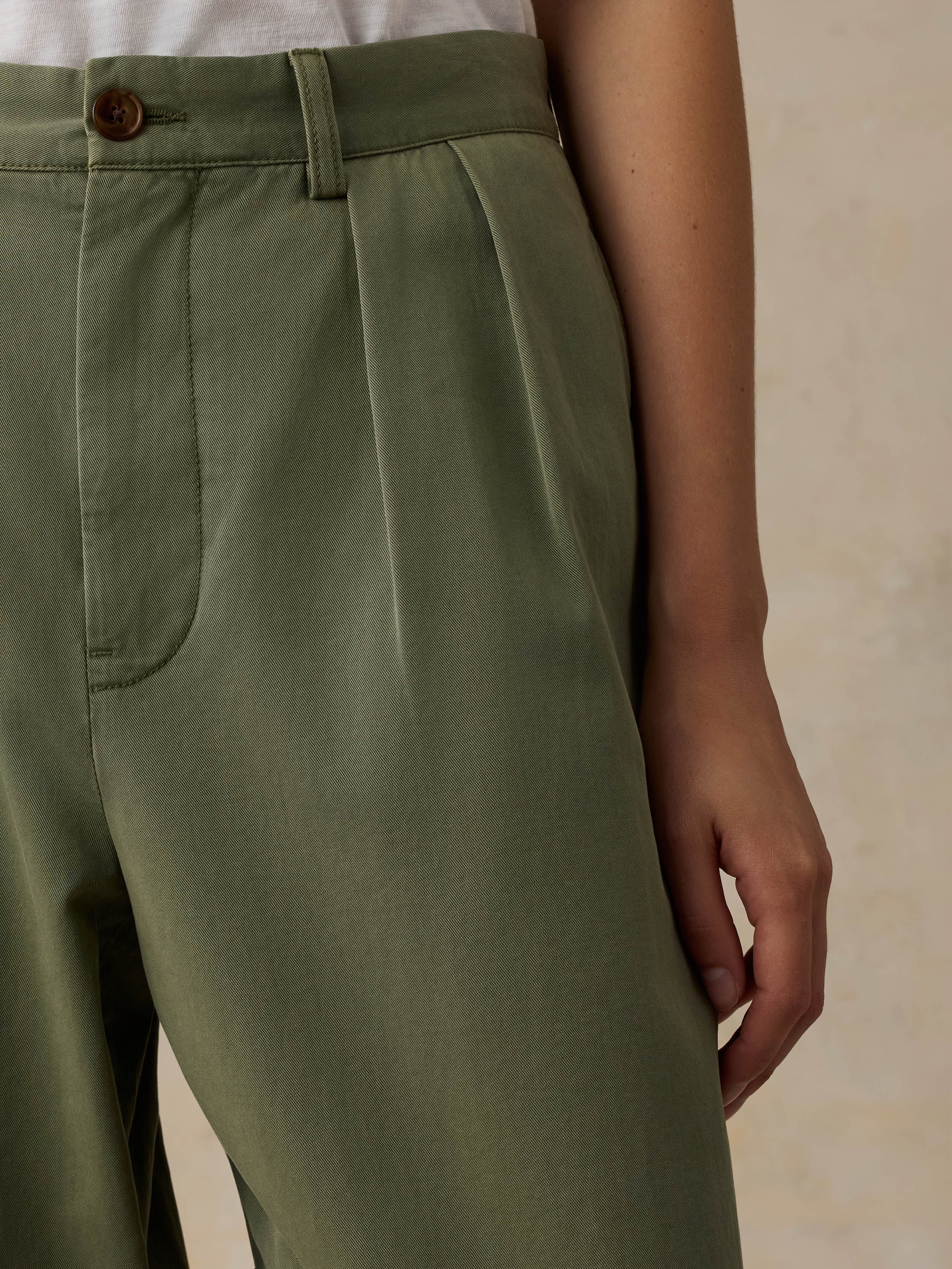 Woman wearing a white t-shirt and green pants against a beige background