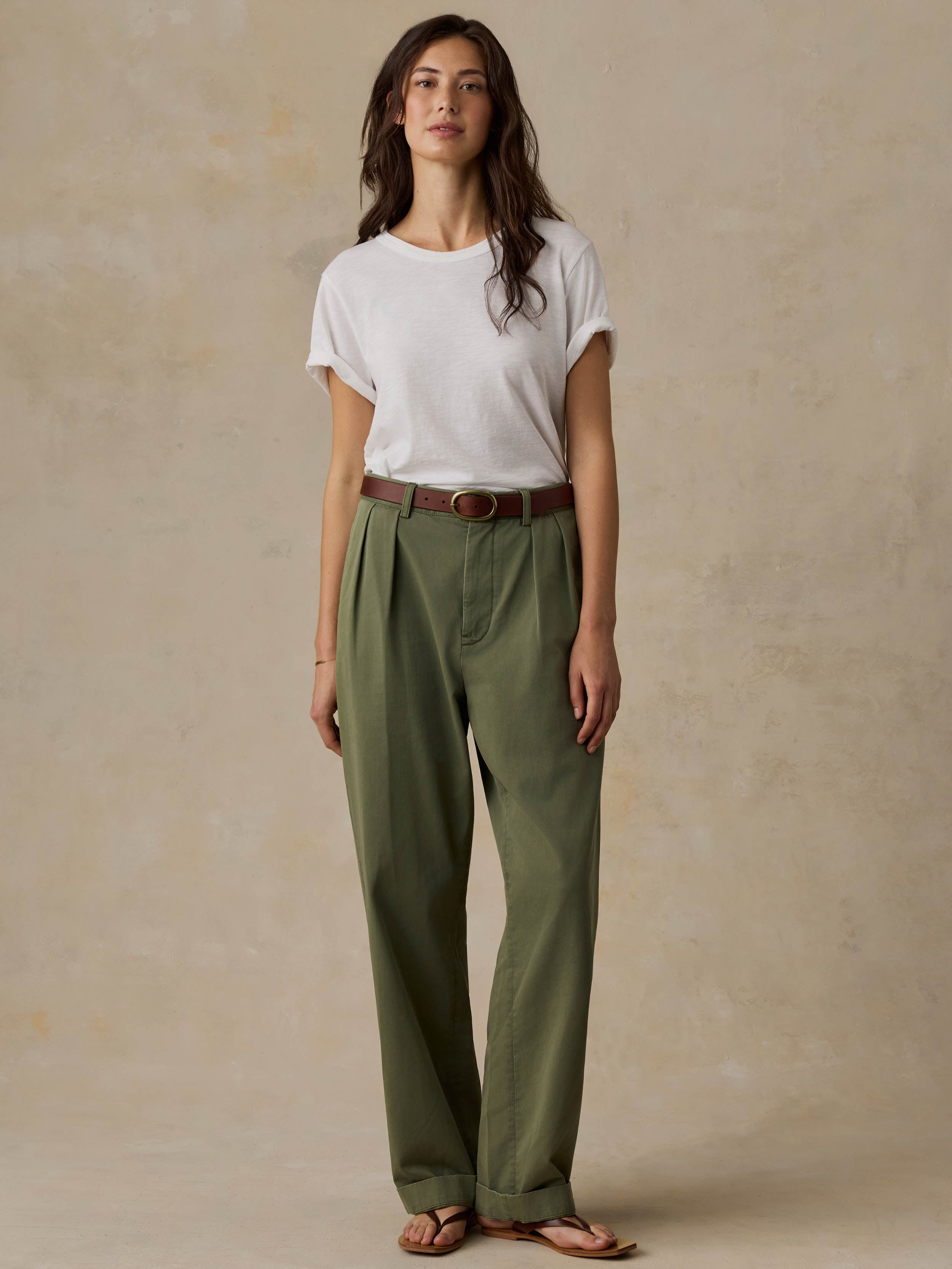 Woman wearing a white t-shirt and green pants against a beige background