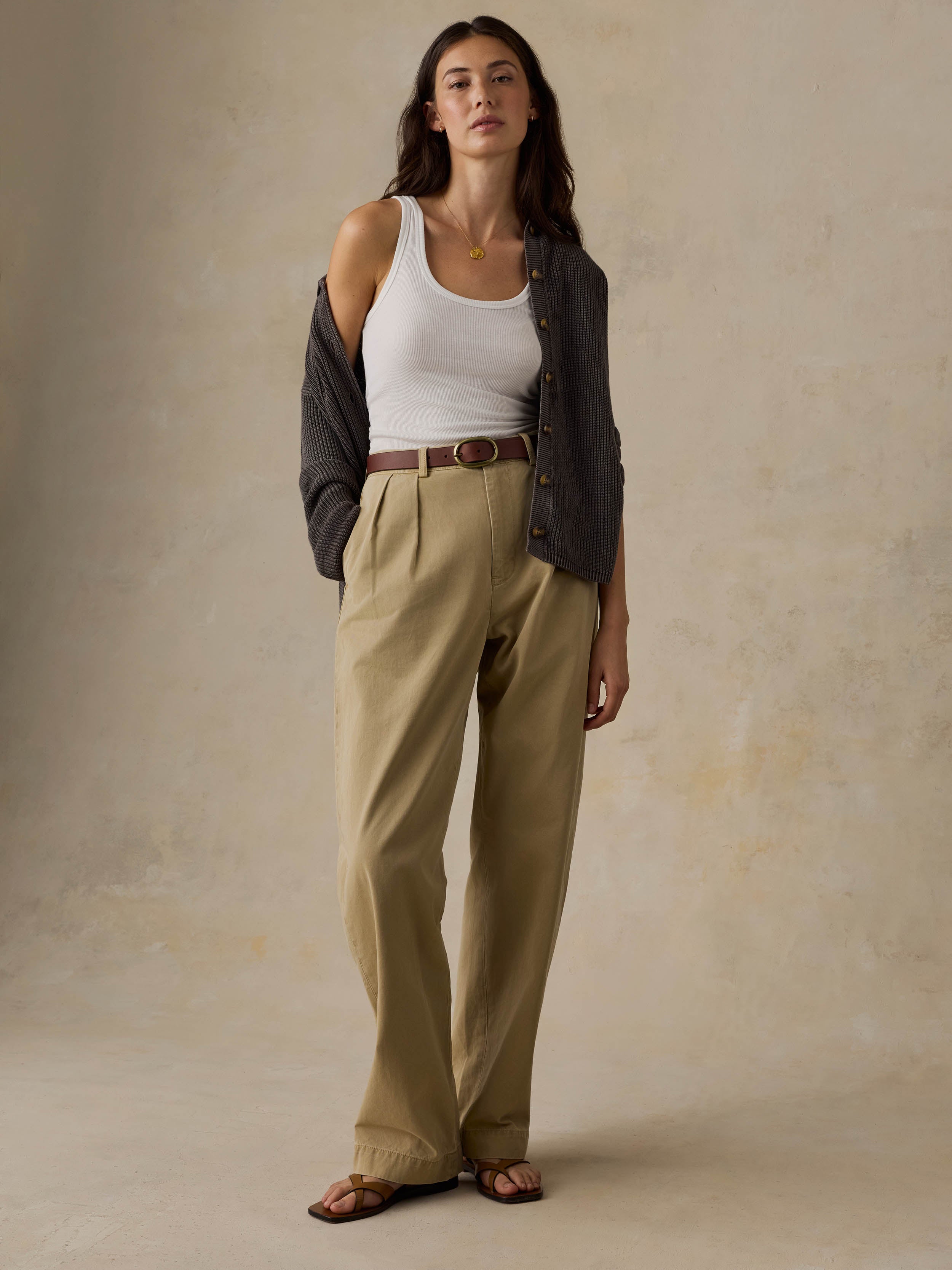 Woman wearing a white tank top and beige pants against a beige background