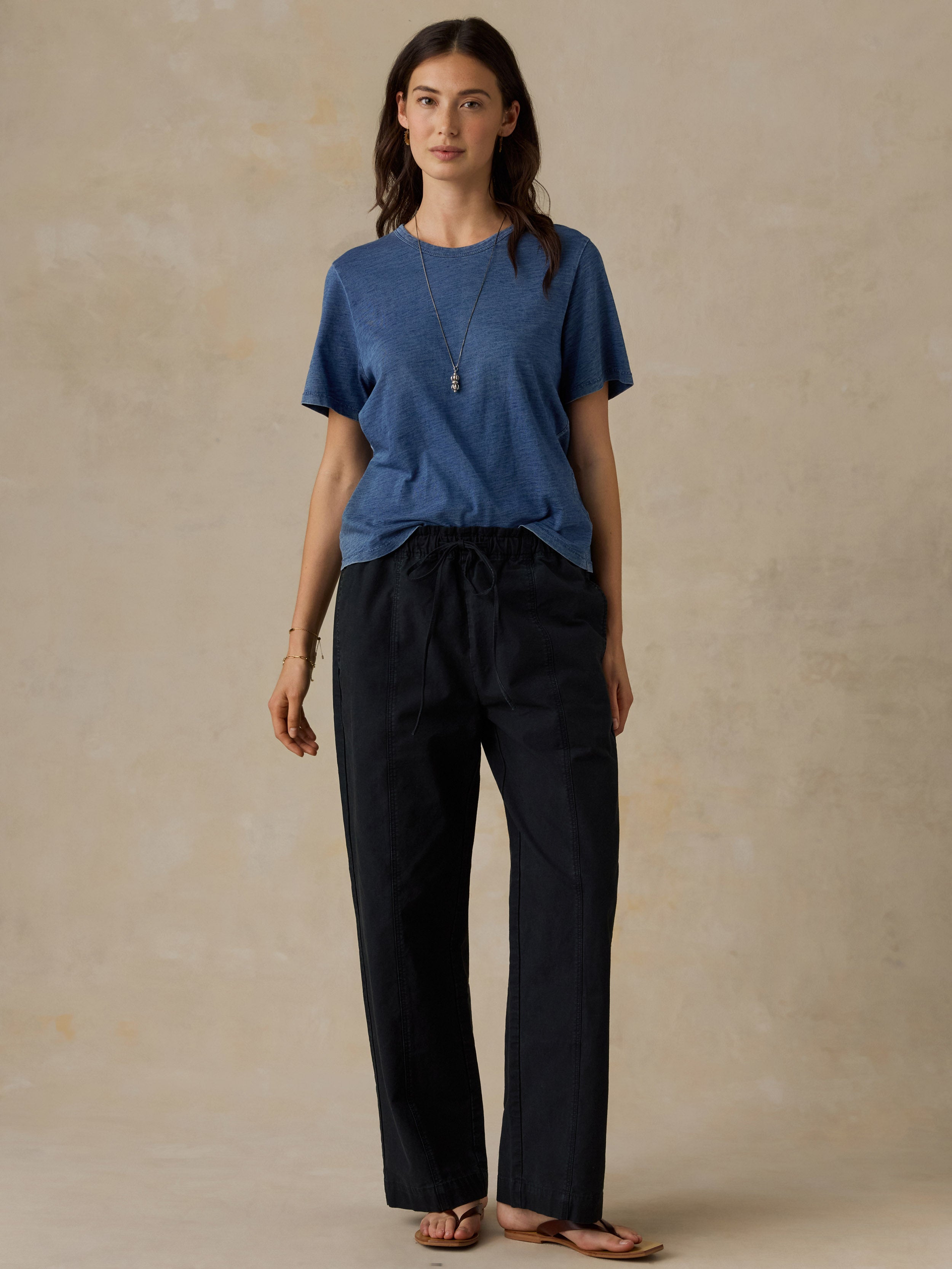 Woman wearing a blue t-shirt and black drawstring pants against a beige background