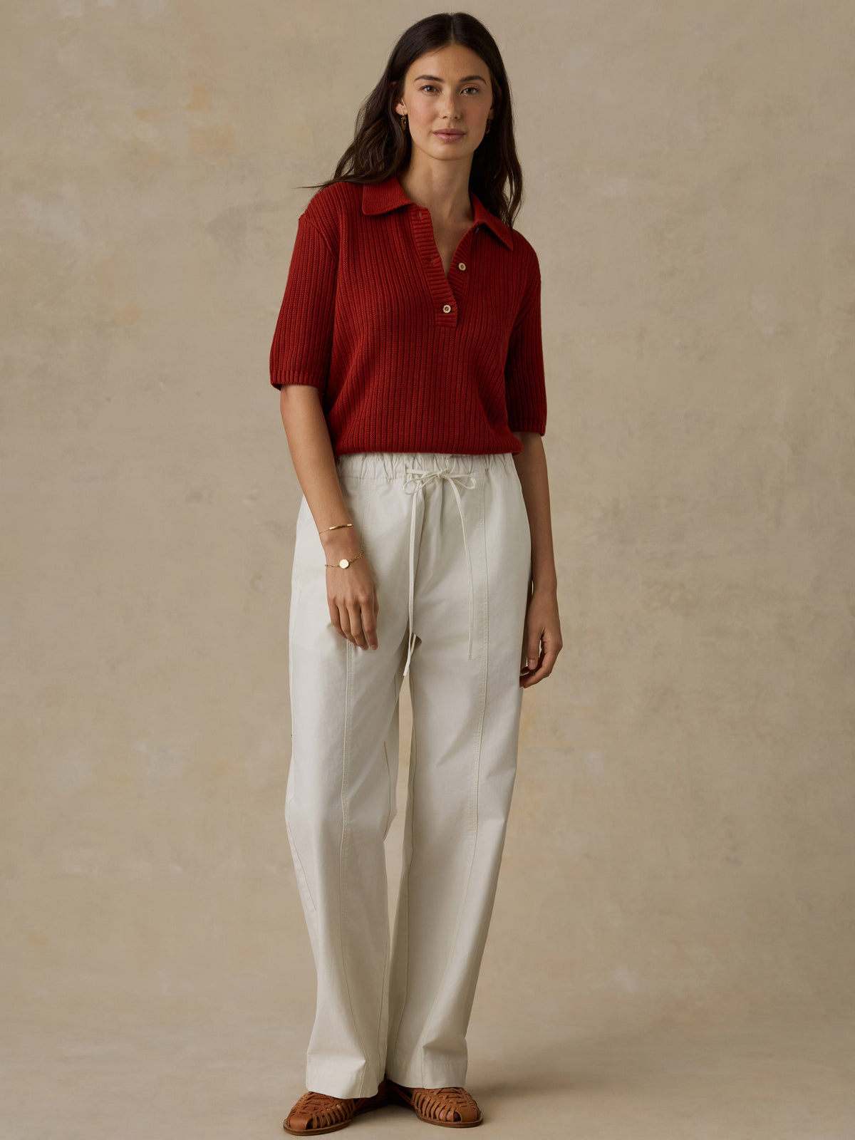 Woman wearing a red knit polo shirt and white drawstring pants against a beige background, image 3 of 6