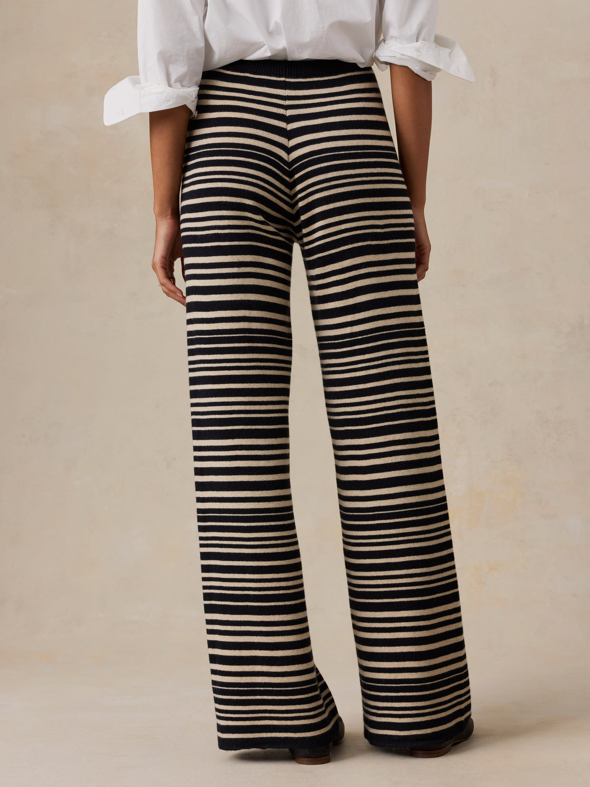 Woman wearing a white button down shirt and black and beige striped pants against a beige studio background, image 4 of 6