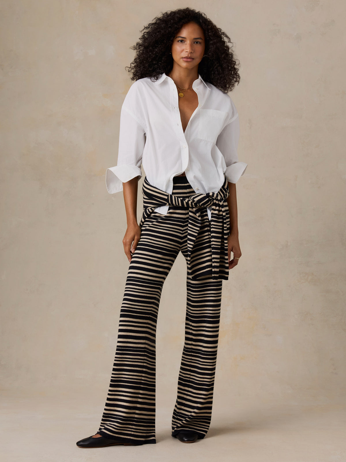 Woman wearing a white button down shirt and black and beige striped pants against a beige studio background, image 6 of 6