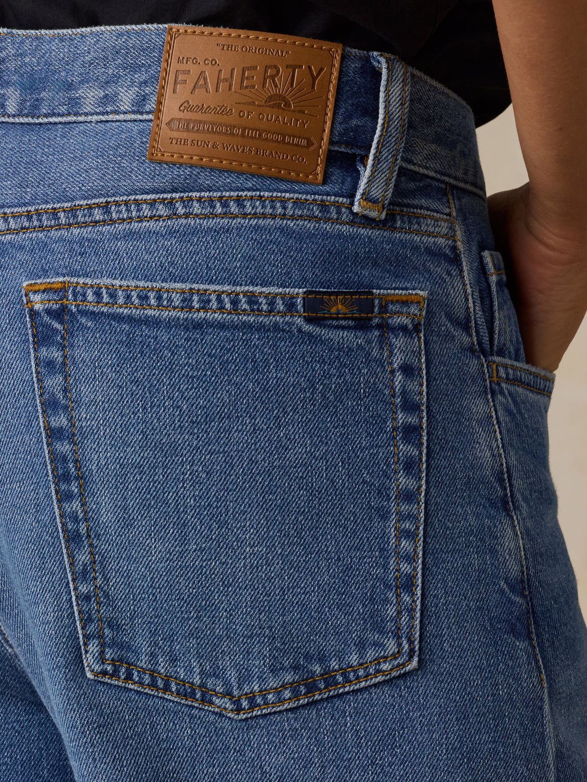 Close-up back view of a woman wearing blue denim jeans with a white top, showing the back pockets and a tan leather waistband patch., image 3 of 6