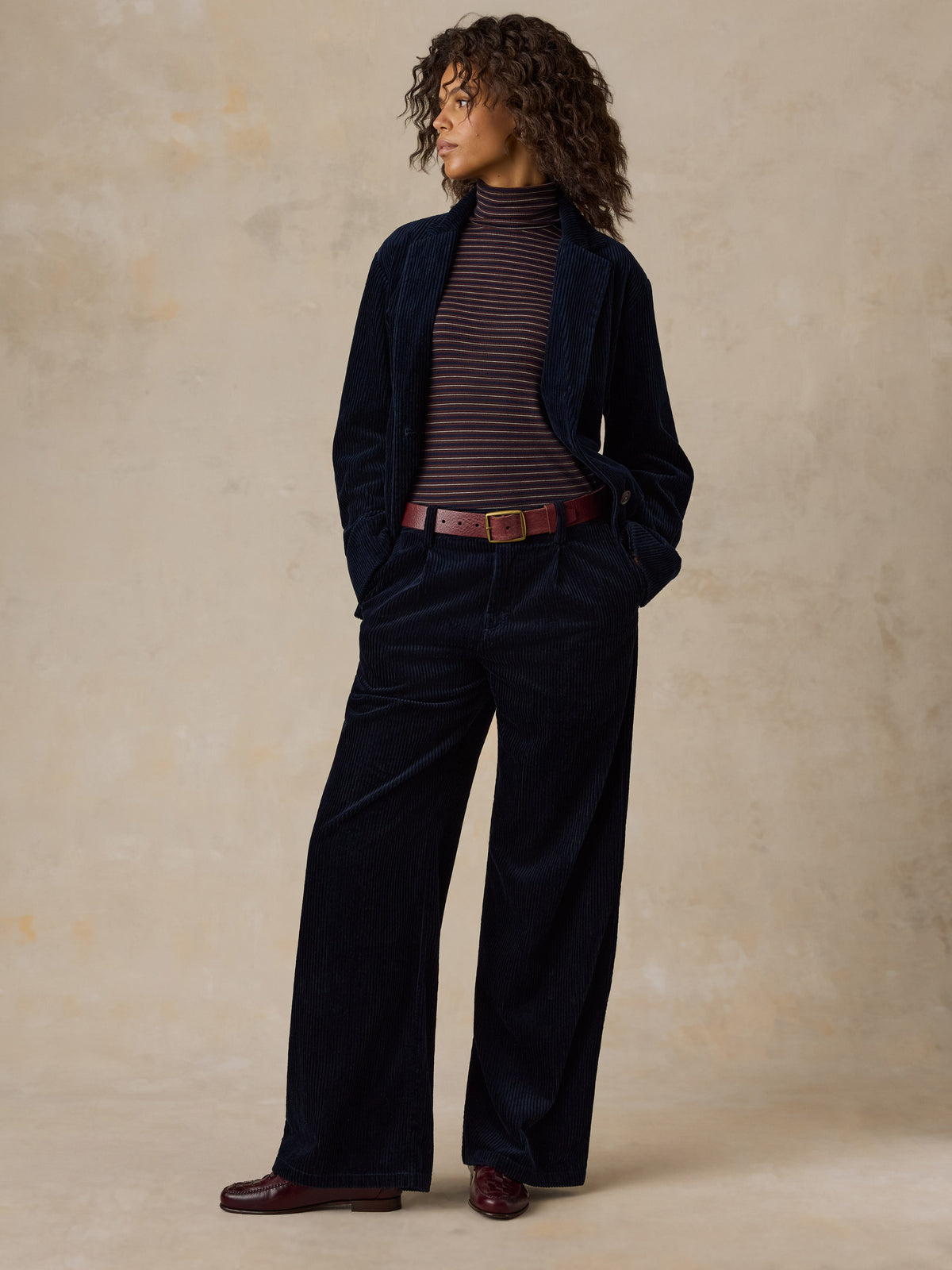 A woman wearing a dark navy corduroy suit over a striped turtleneck, image 7 of 7