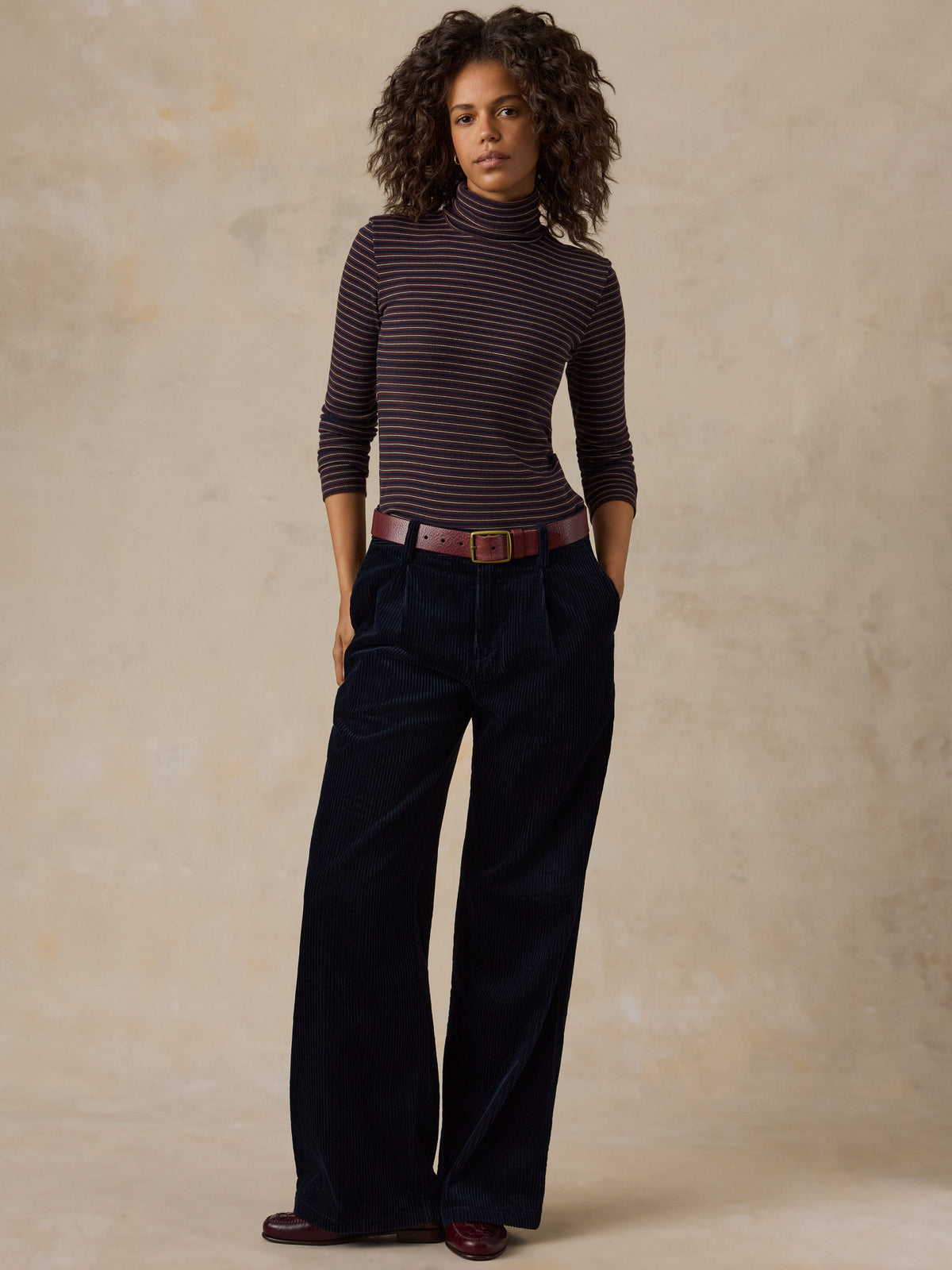 A woman wearing a striped turtleneck and dark navy corduroy pants, image 1 of 7