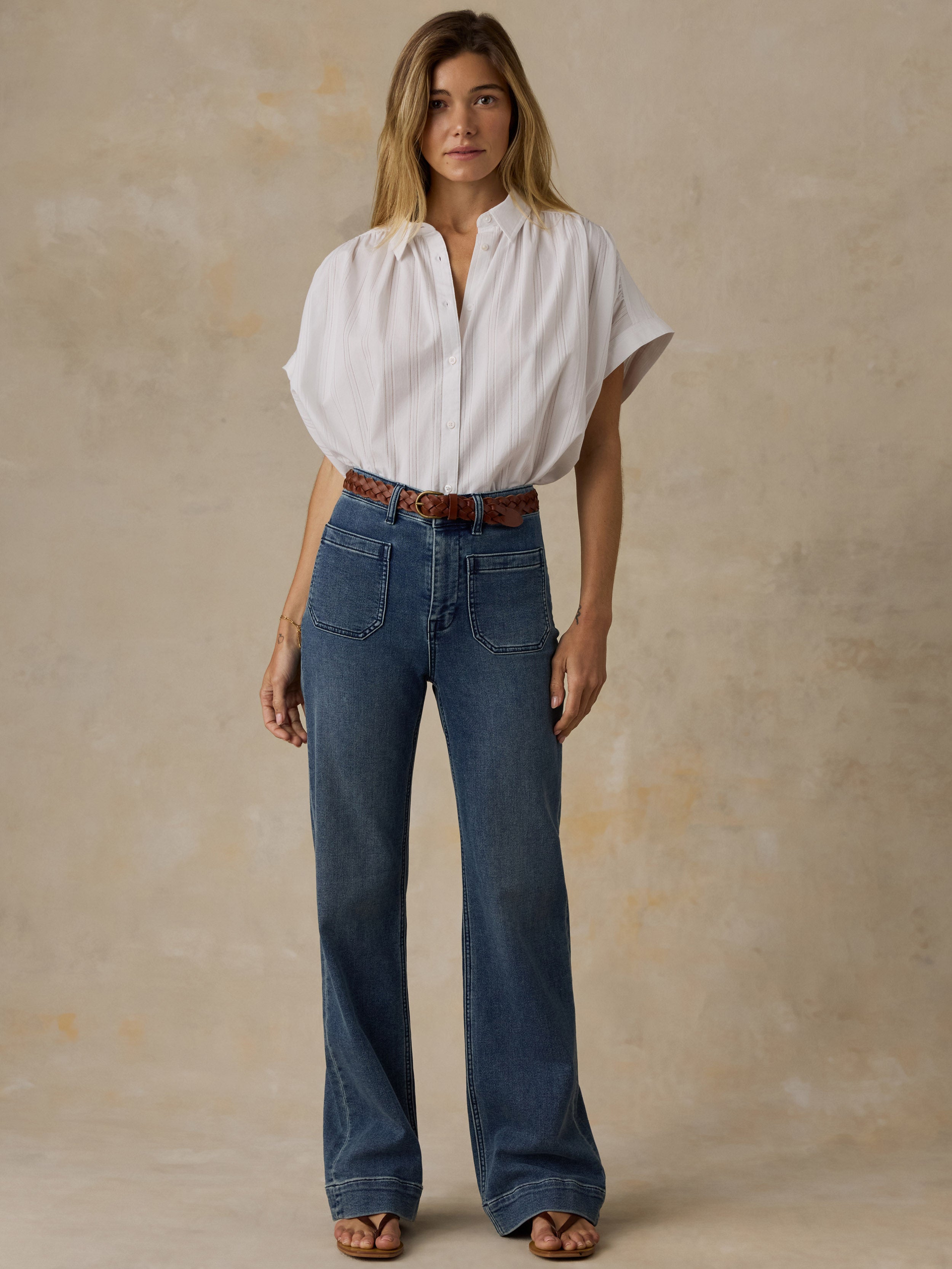 Woman wearing a white top and high waisted blue jeans against a beige background