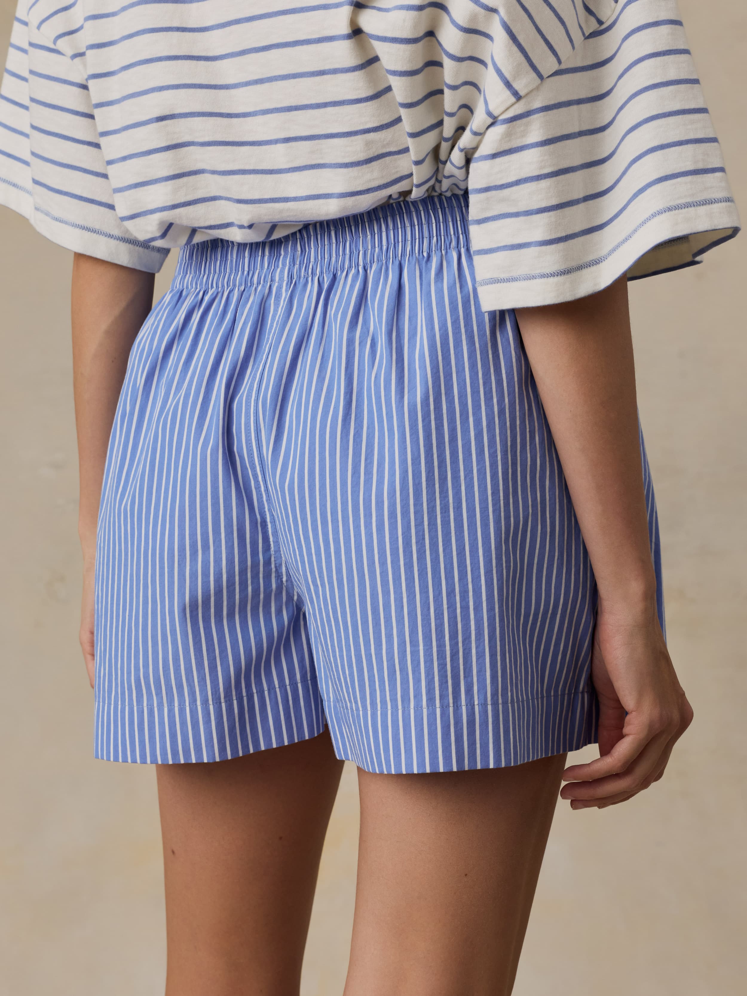 Woman is wearing a striped t-shirt and shirt shorts against a beige background