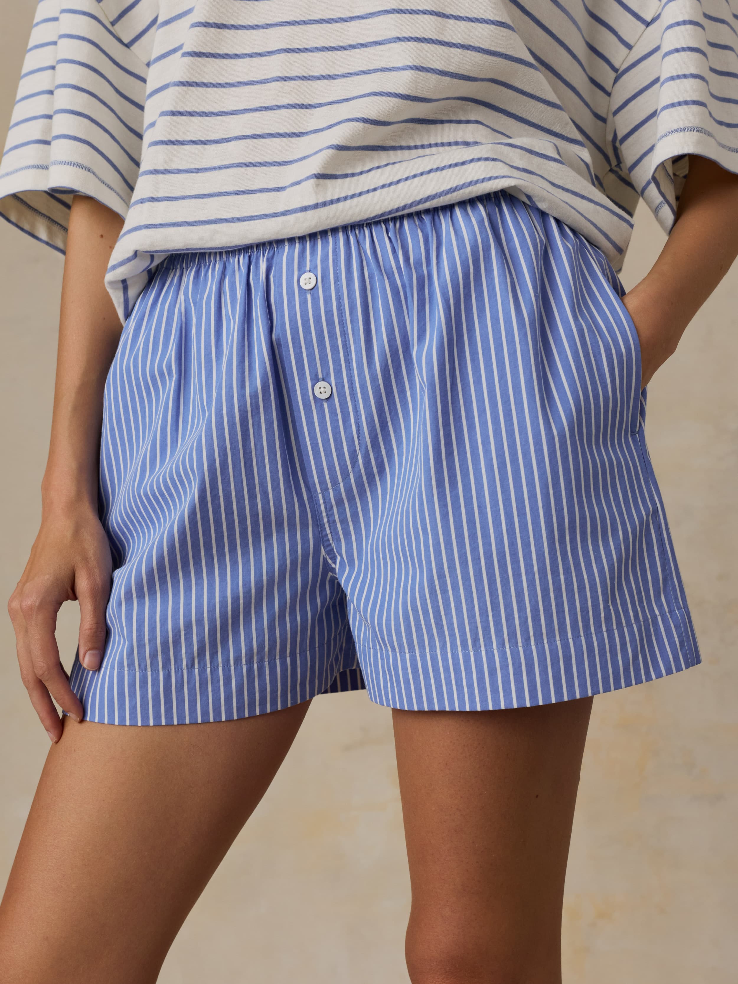 Woman is wearing a striped t-shirt and shirt shorts against a beige background