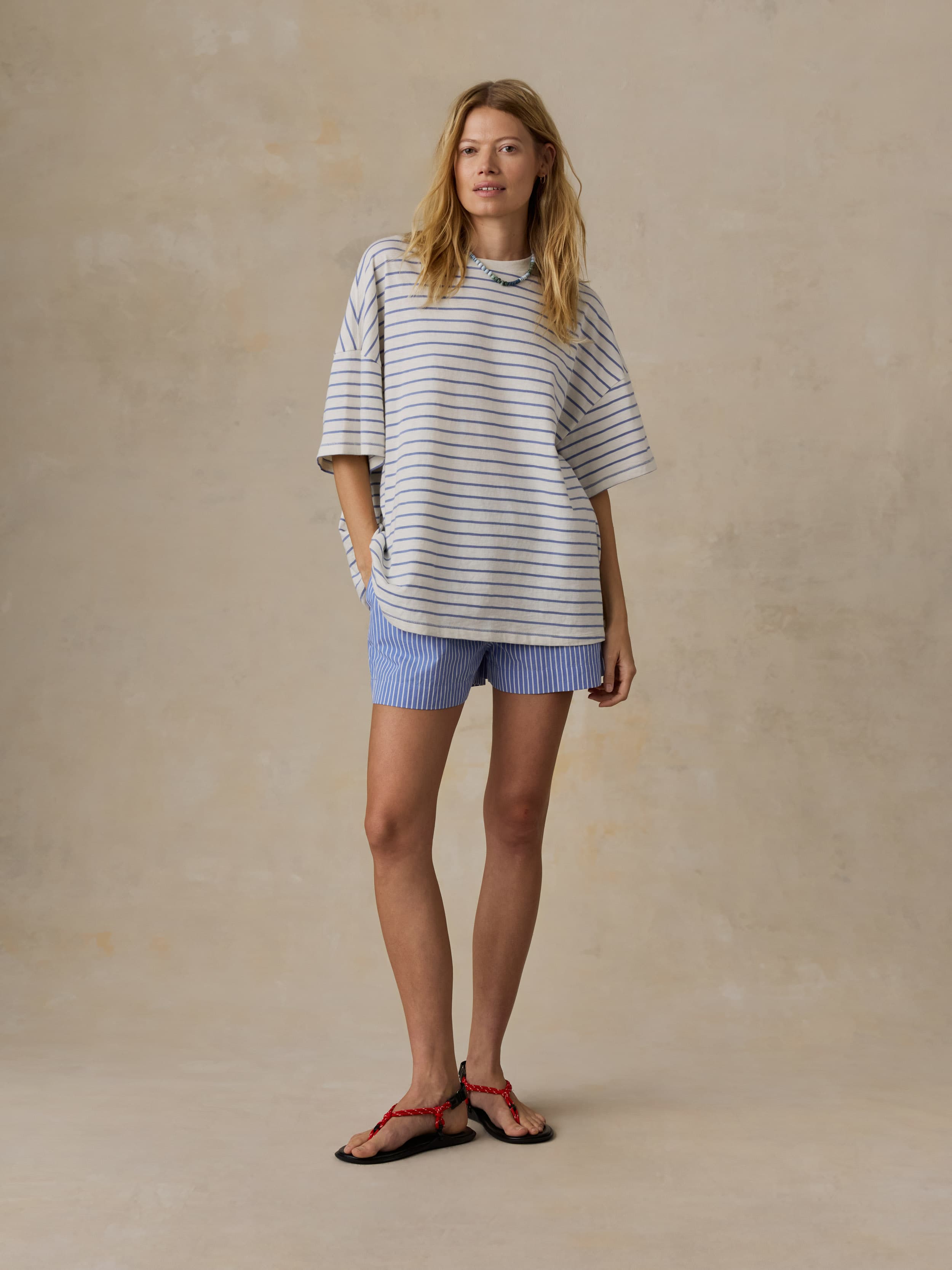 Woman is wearing a striped t-shirt and shirt shorts against a beige background