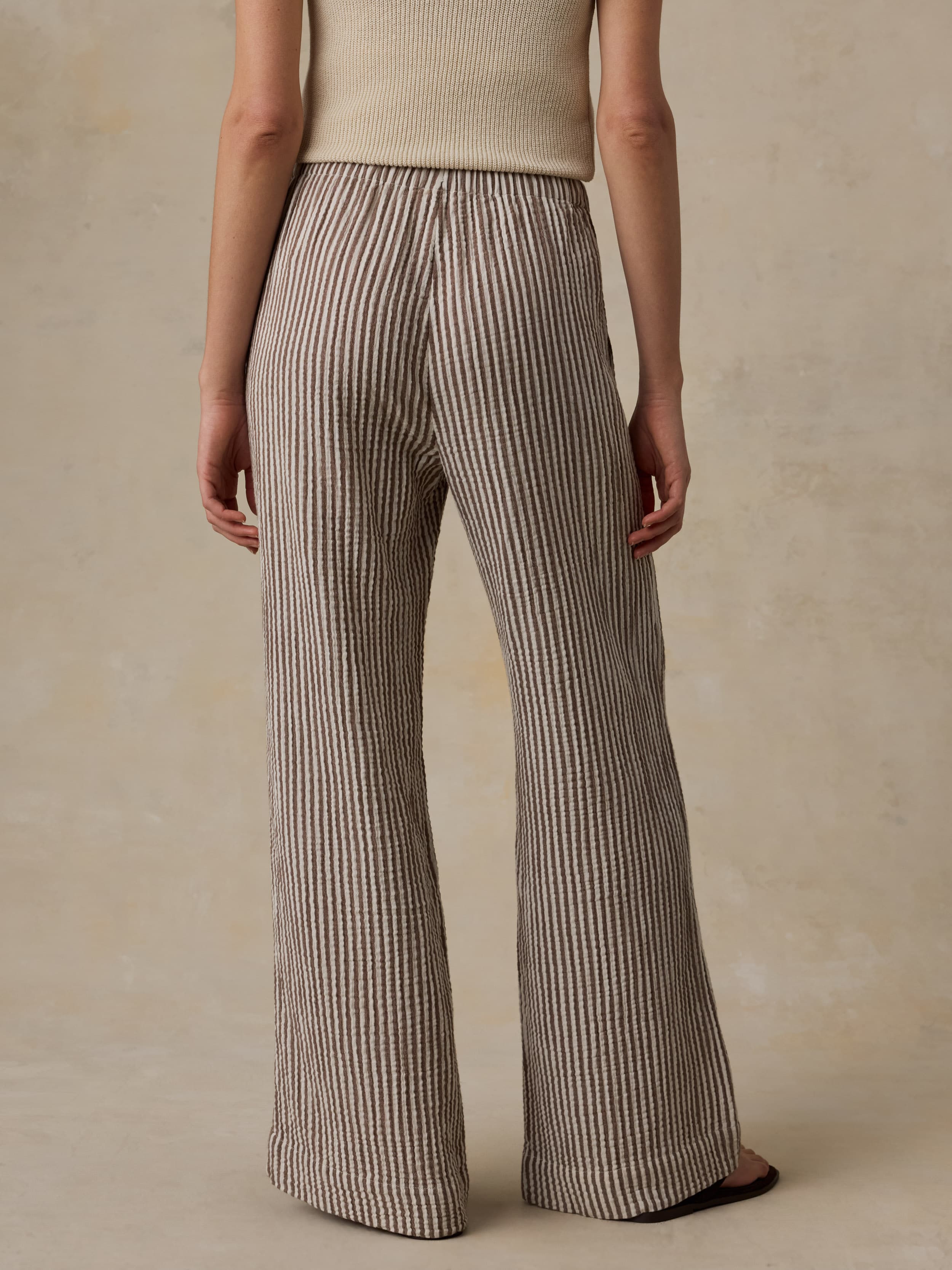 Woman wearing a beige tank top and striped pants against a beige background