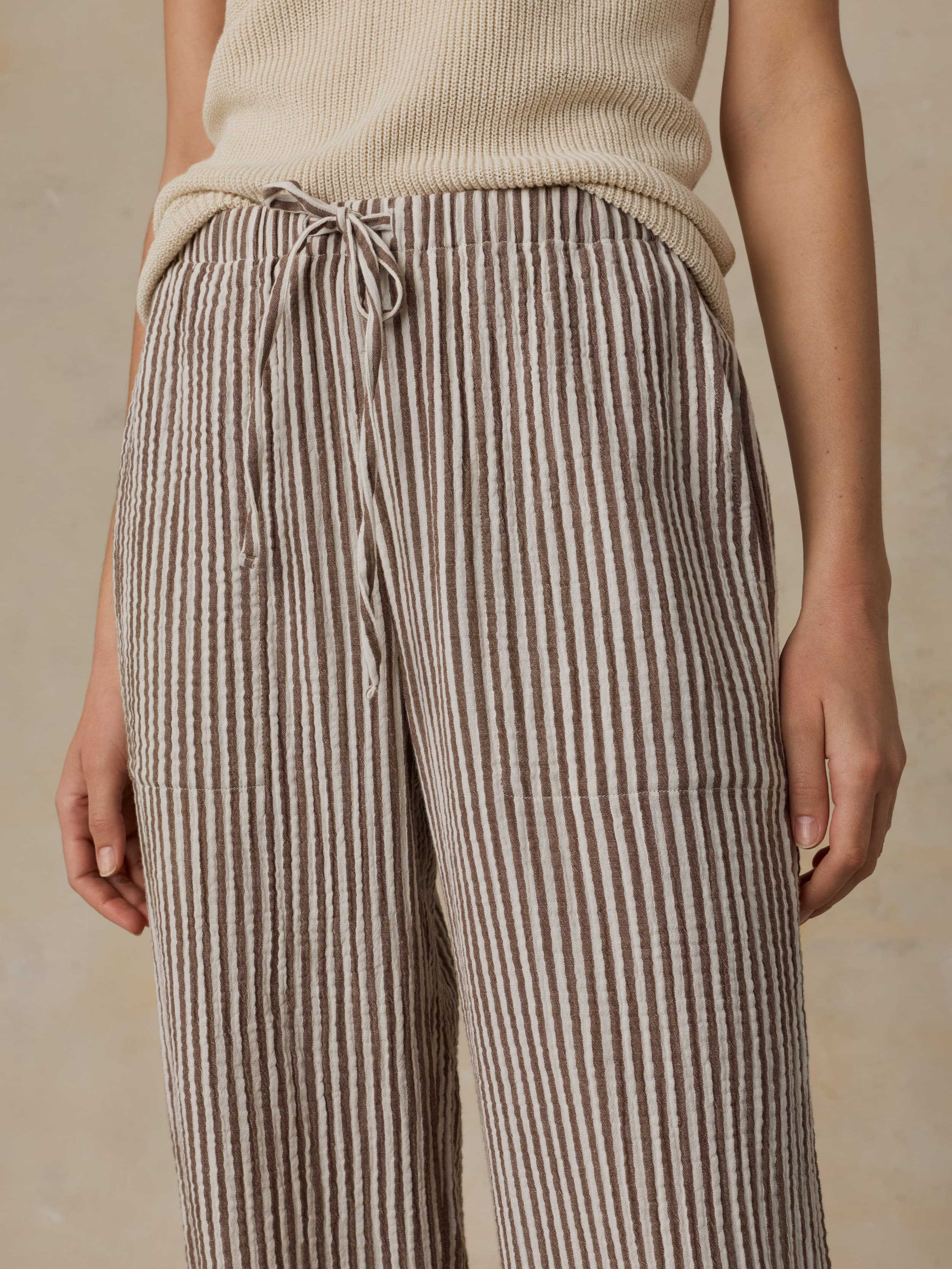 Woman wearing a beige tank top and striped pants against a beige background
