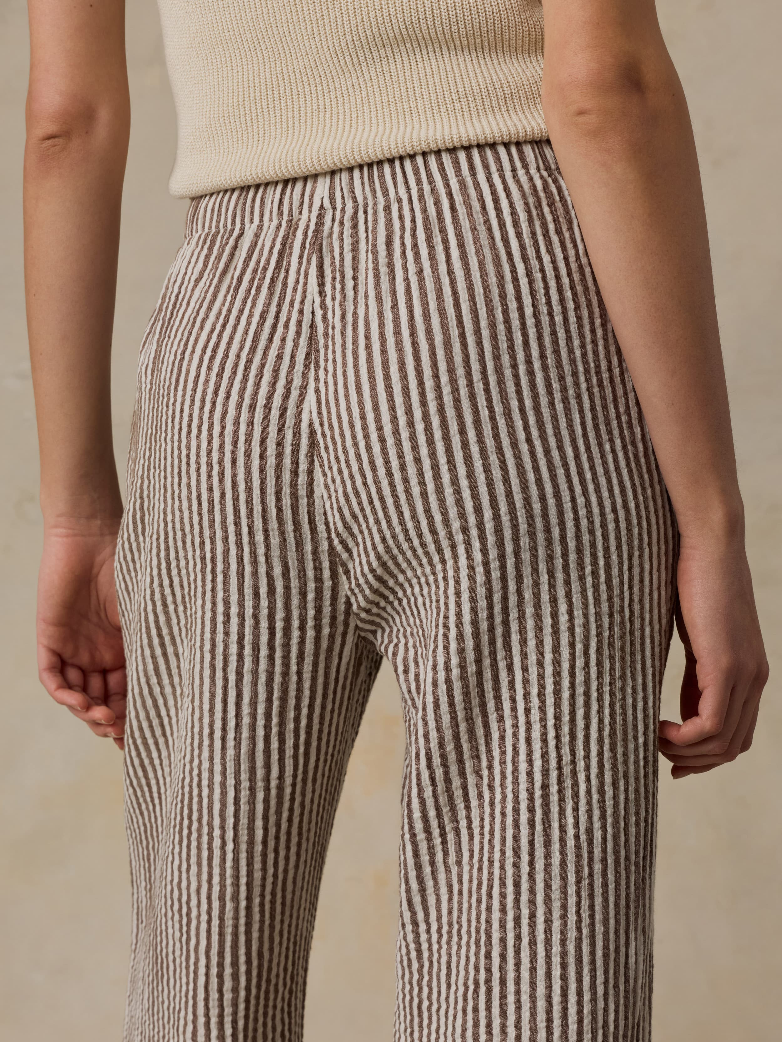Woman wearing a beige tank top and striped pants against a beige background