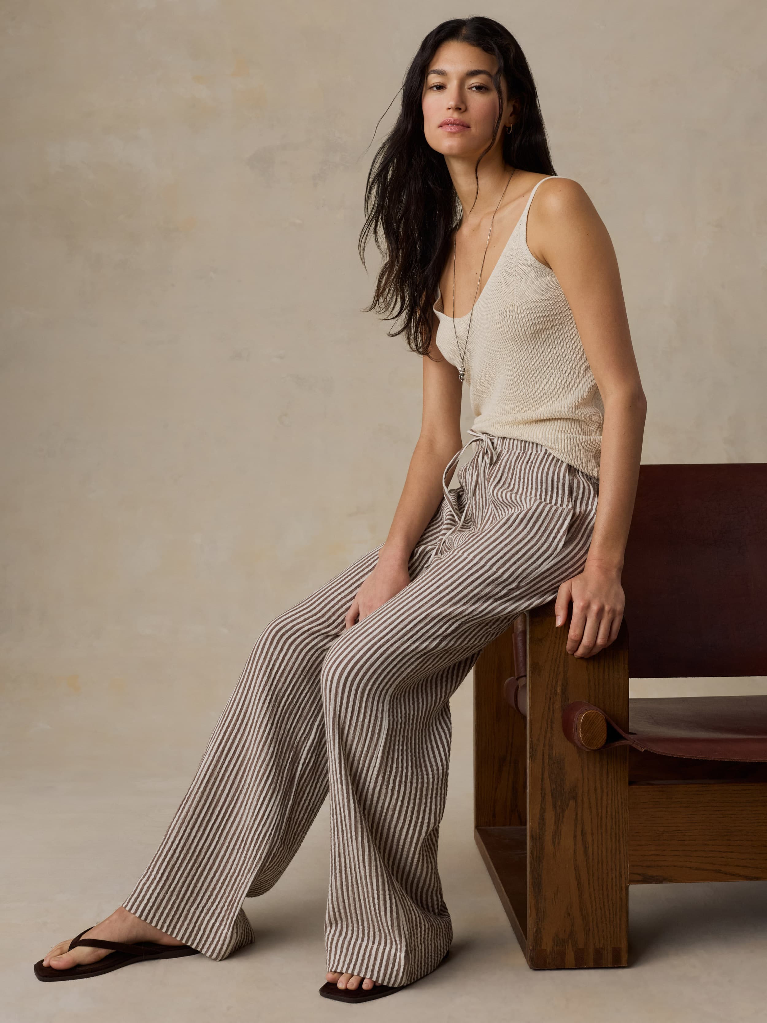 Woman wearing a beige tank top and striped pants against a beige background