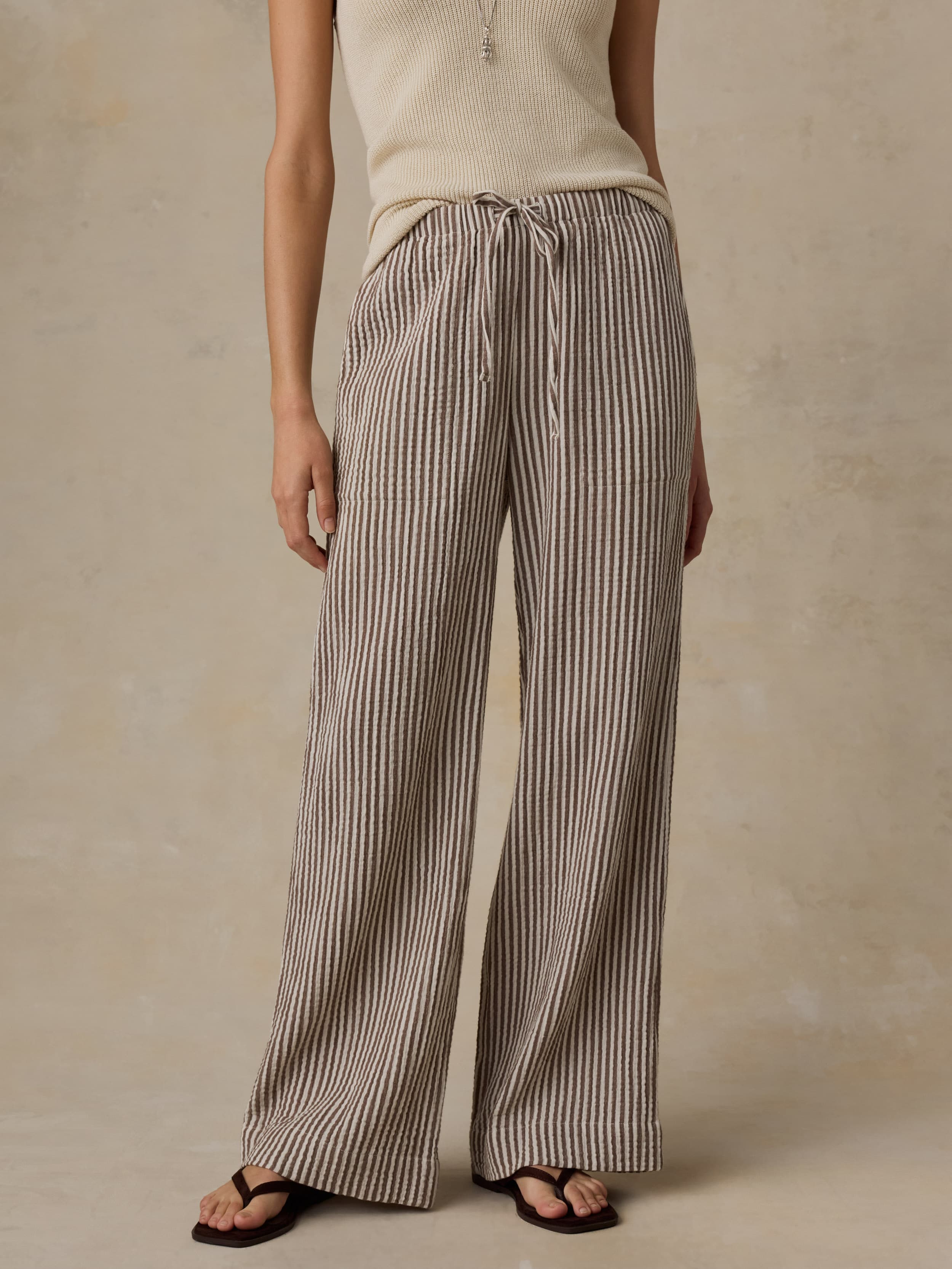 Woman wearing a beige tank top and striped pants against a beige background