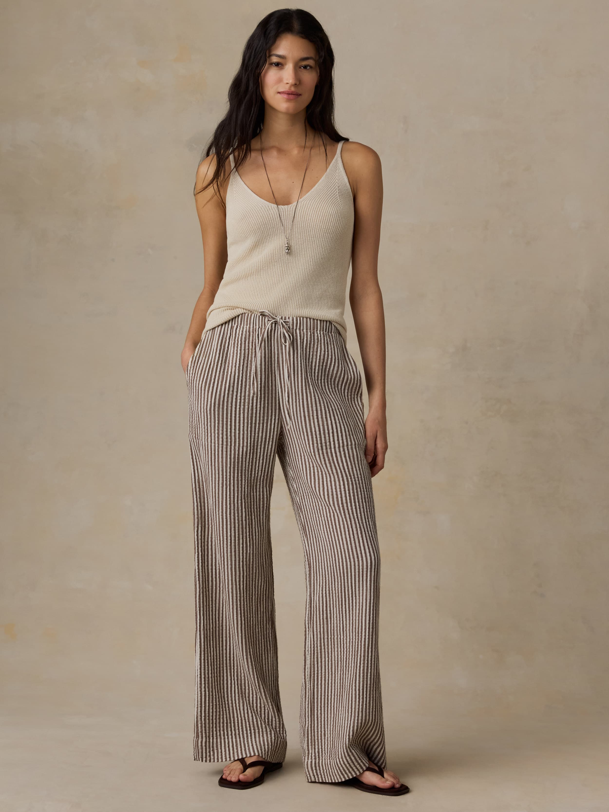Woman wearing a beige tank top and striped pants against a beige background