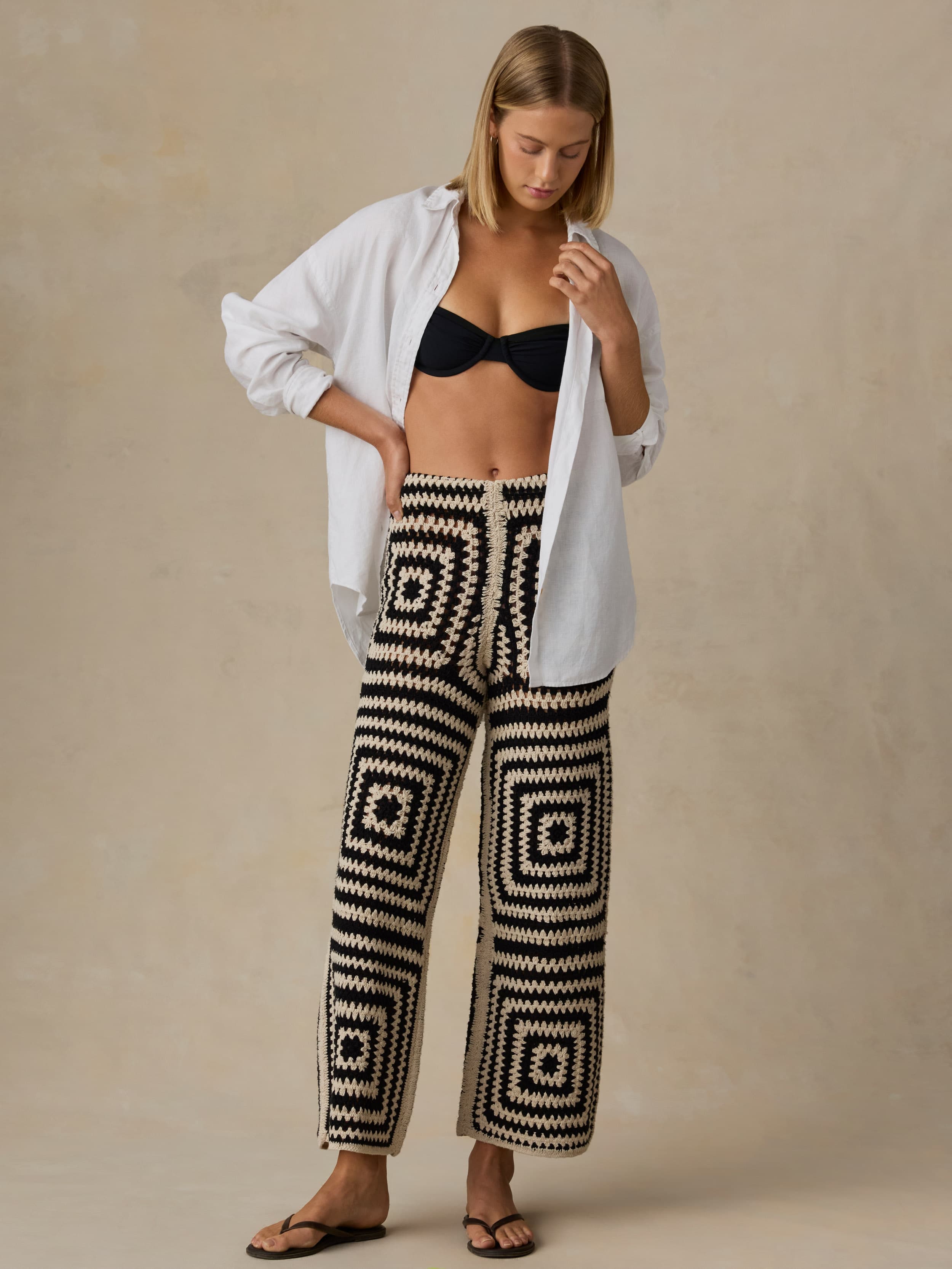Woman wearing a black and white patterned pants with a white shirt over a black top on a beige background