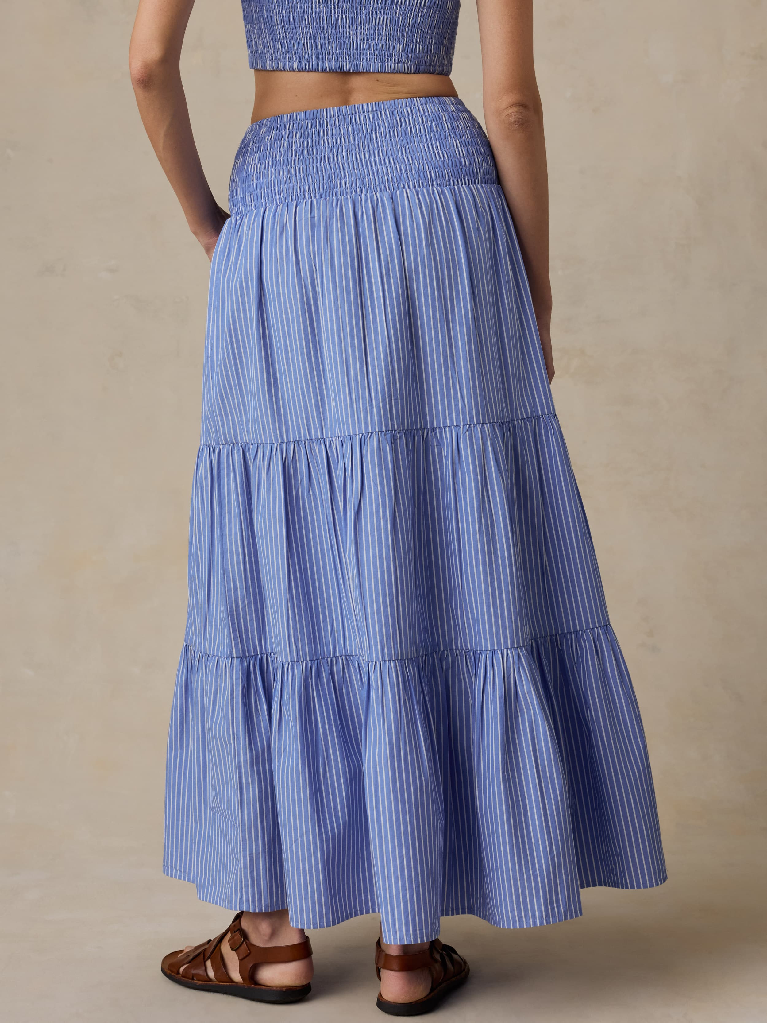 Woman is wearing a striped maxi skirt and matching bandeau top against a beige background