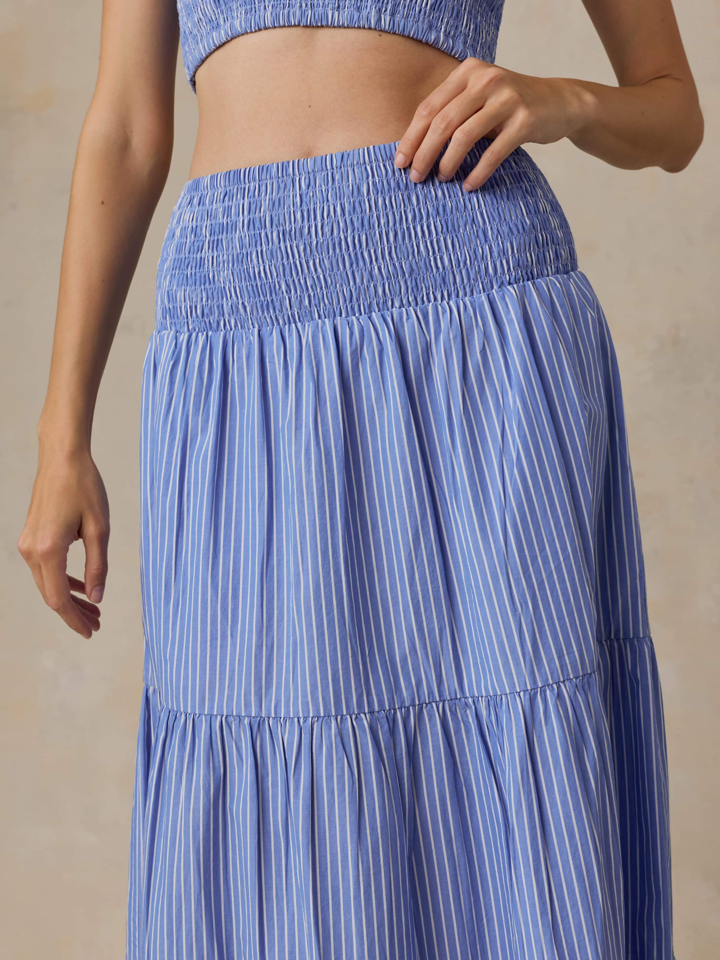 Woman is wearing a striped maxi skirt and matching bandeau top against a beige background
