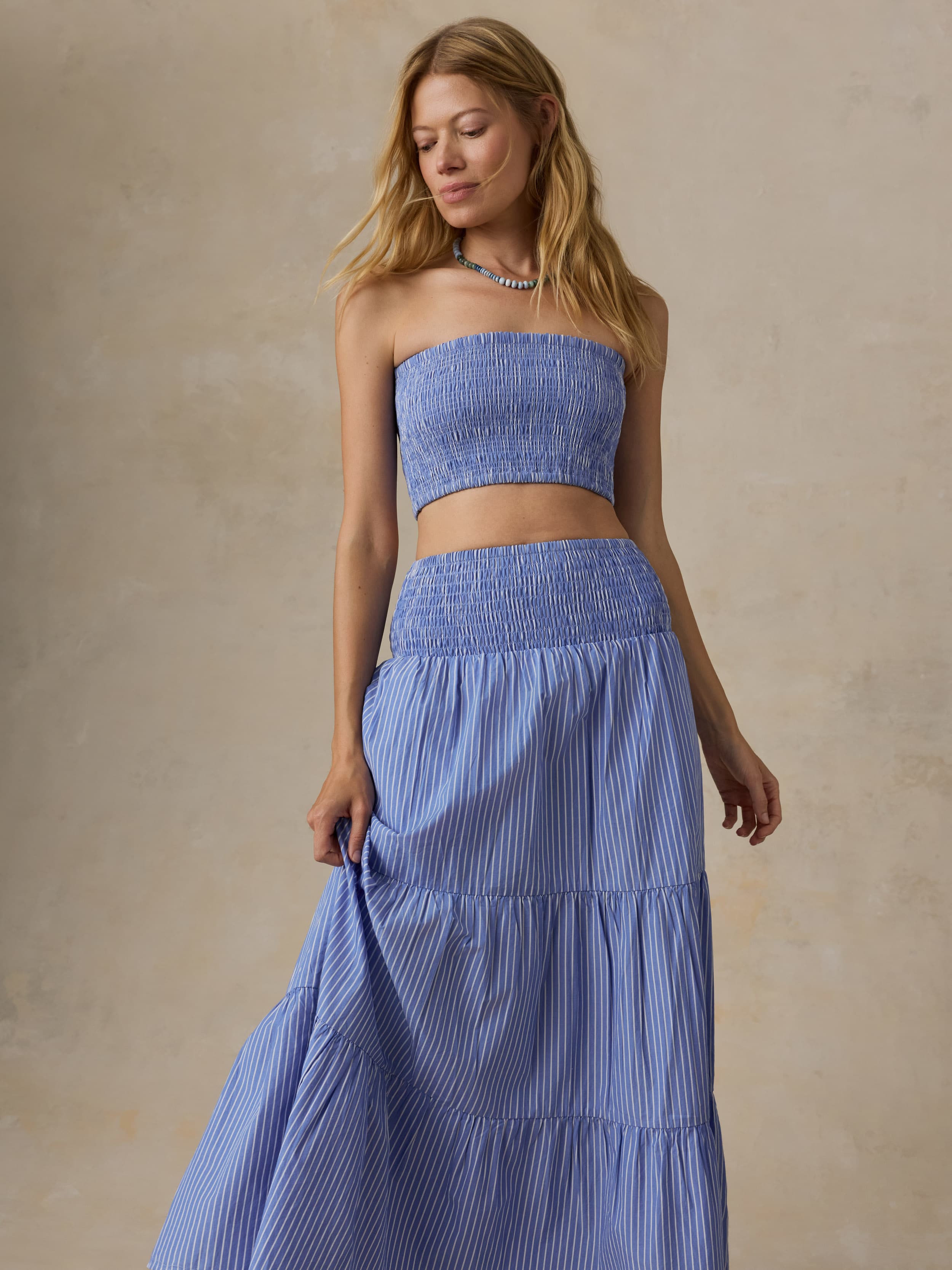 Woman is wearing a striped maxi skirt and matching bandeau top against a beige background