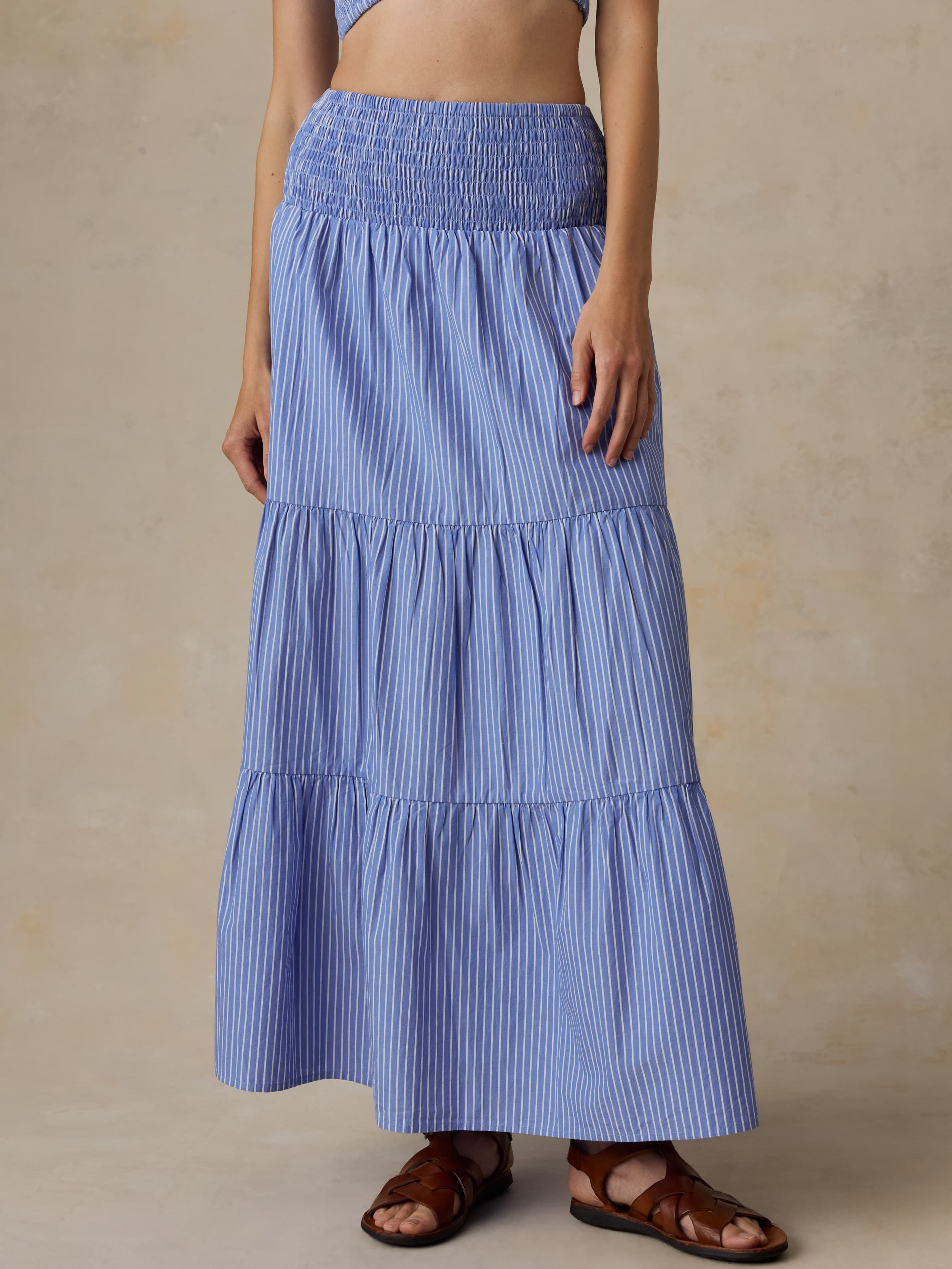 Woman is wearing a striped maxi skirt and matching bandeau top against a beige background