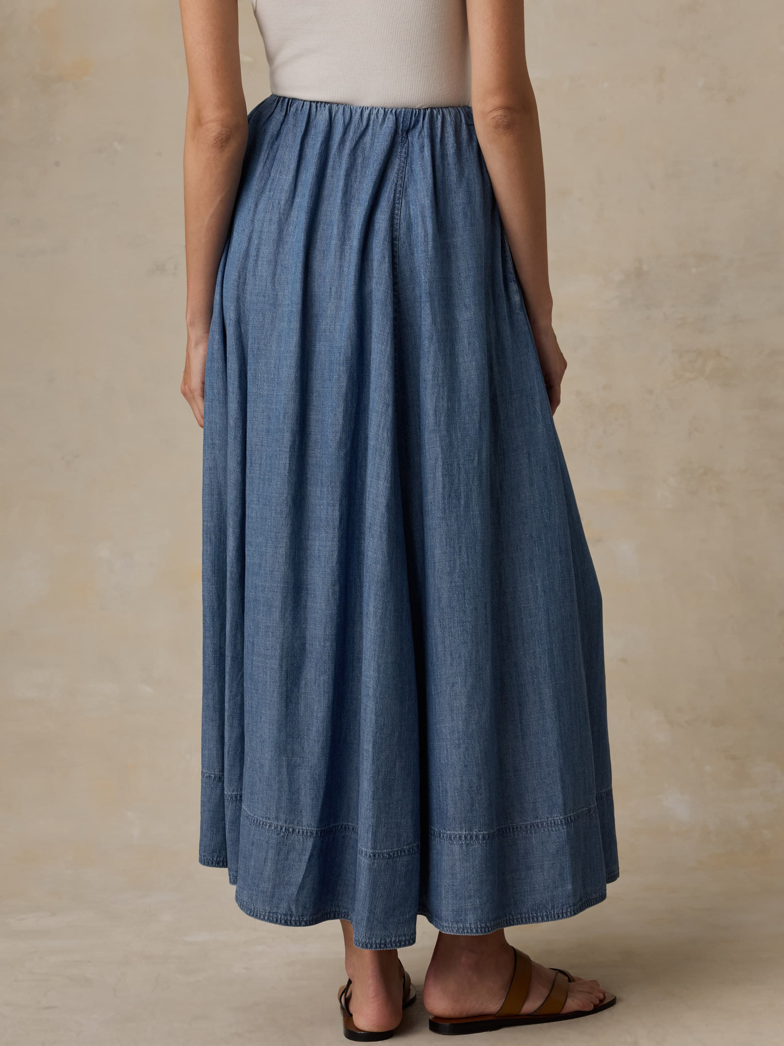 Woman wearing a denim skirt and white tank top against a beige background