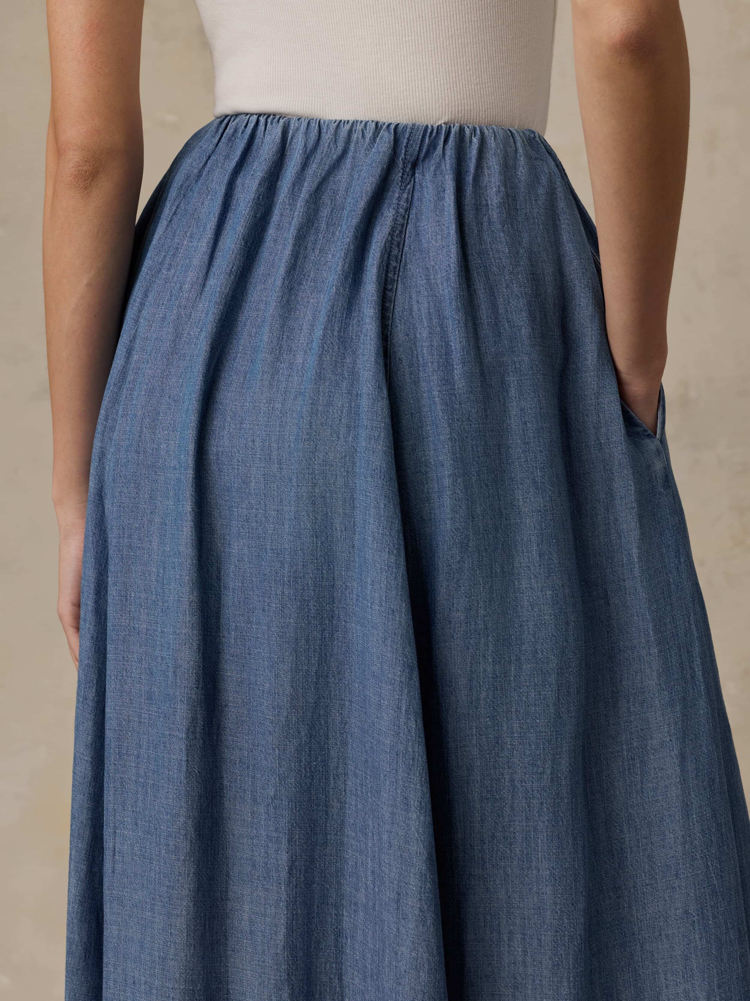 Woman wearing a denim skirt and white tank top against a beige background