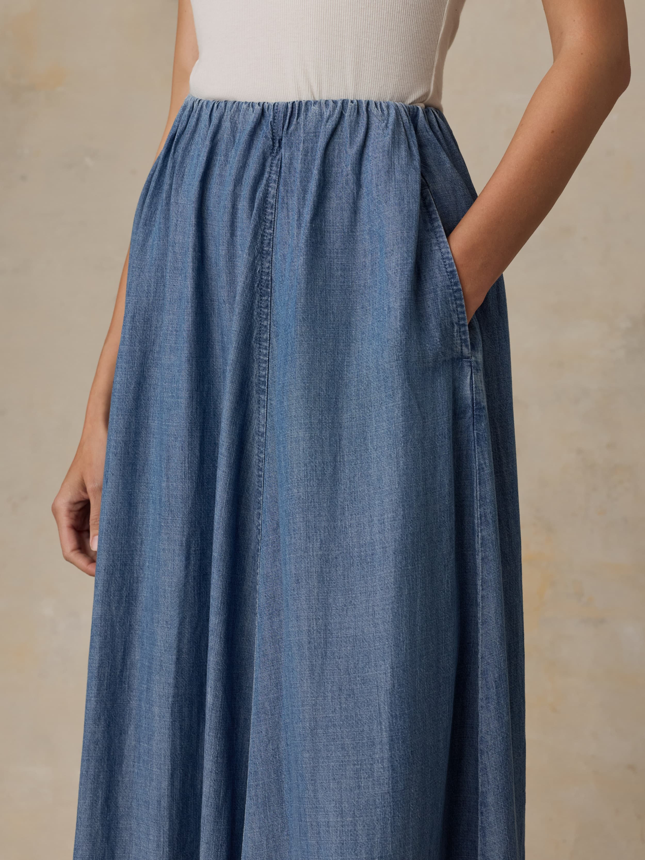 Woman wearing a denim skirt and white tank top against a beige background