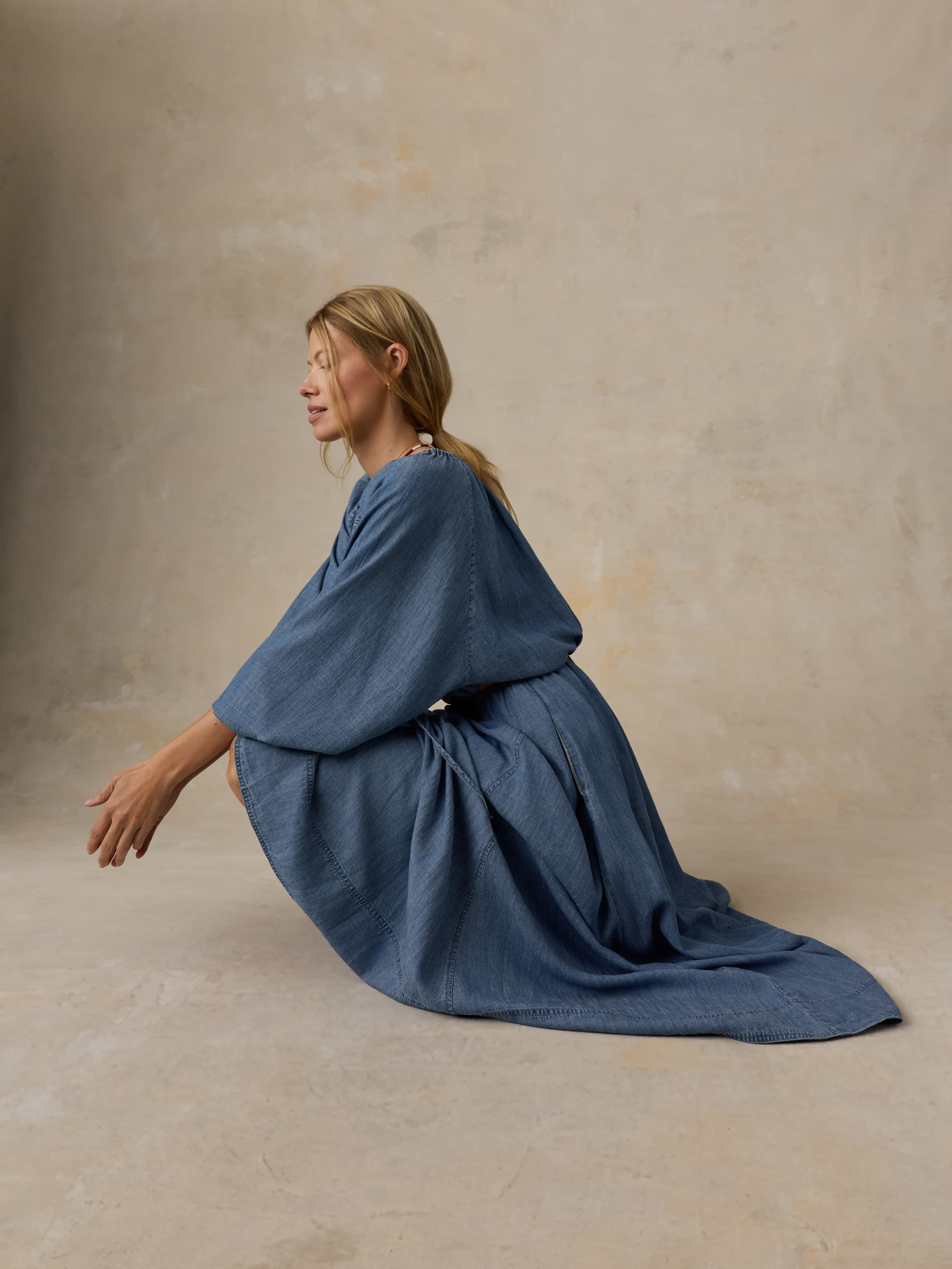 Woman wearing a blue denim top and matching skirt against a beige background