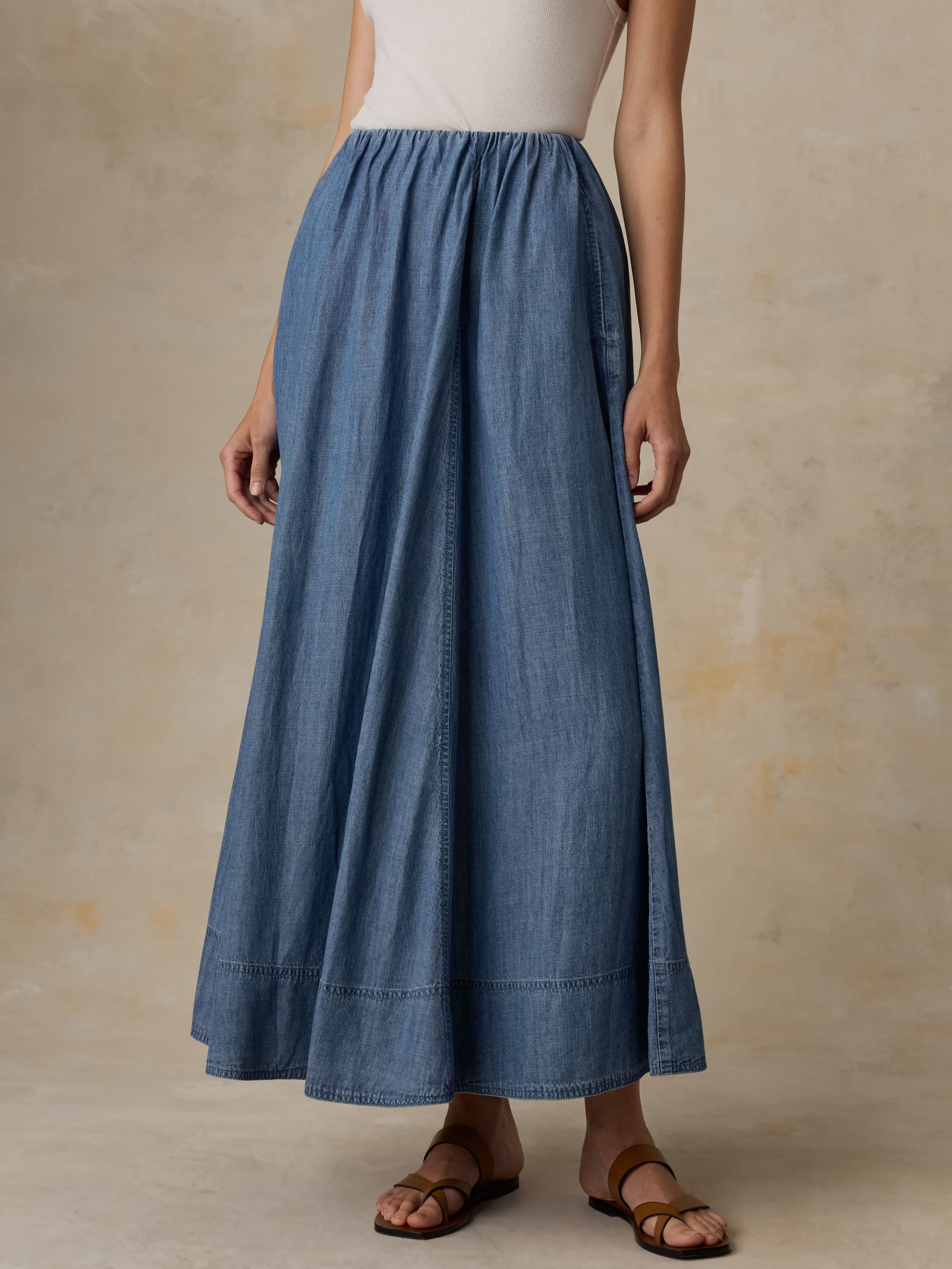 Woman wearing a denim skirt and white tank top against a beige background