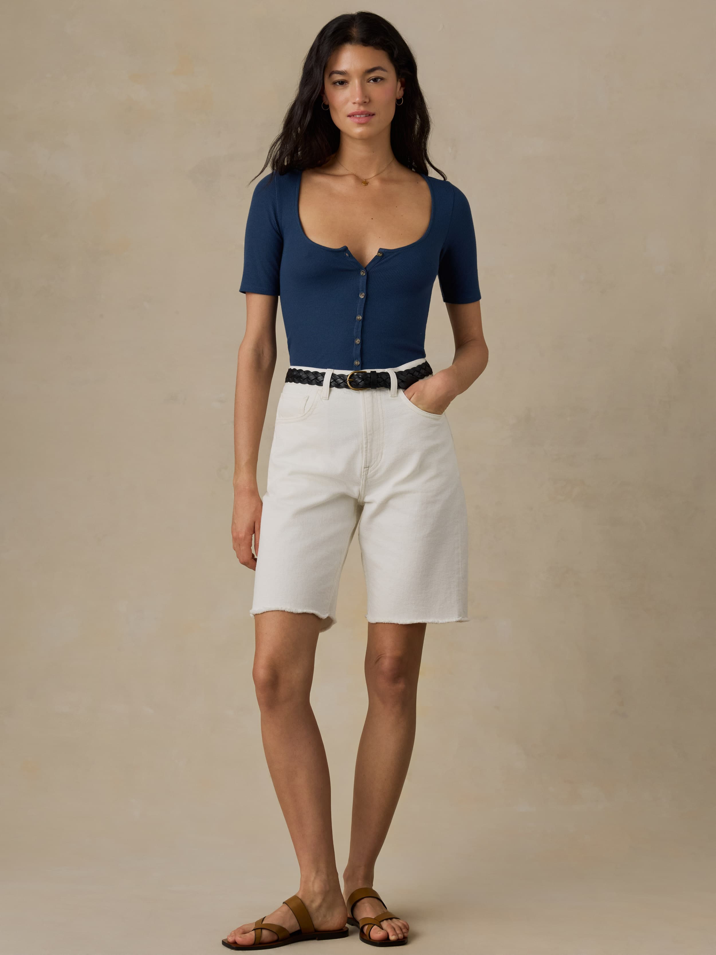 Woman wearing white denim shorts and a blue shirt against a beige background