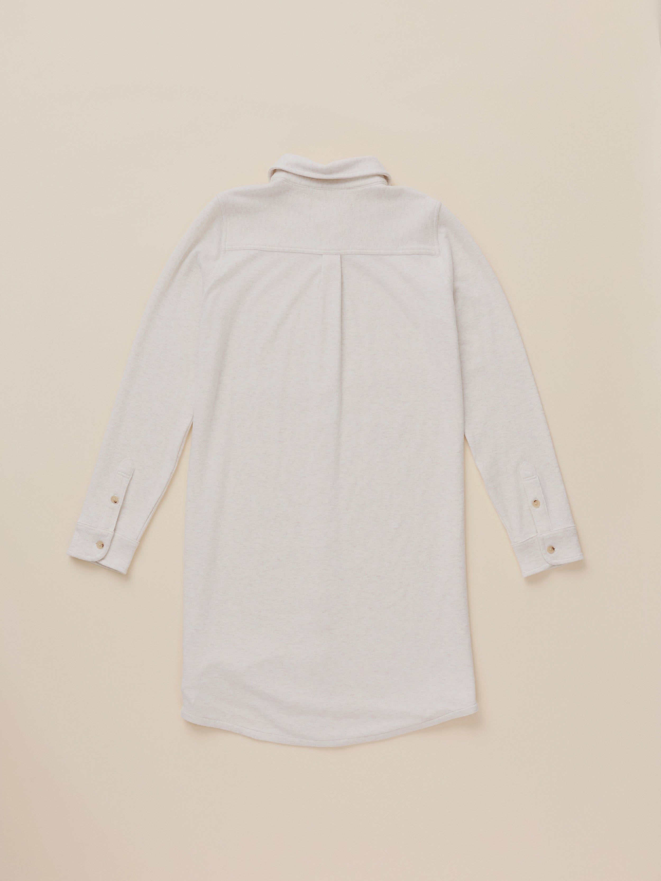 A light beige long-sleeve shirt dress shown from the back, featuring a buttoned collar and button cuffs, laid flat against a solid beige background.