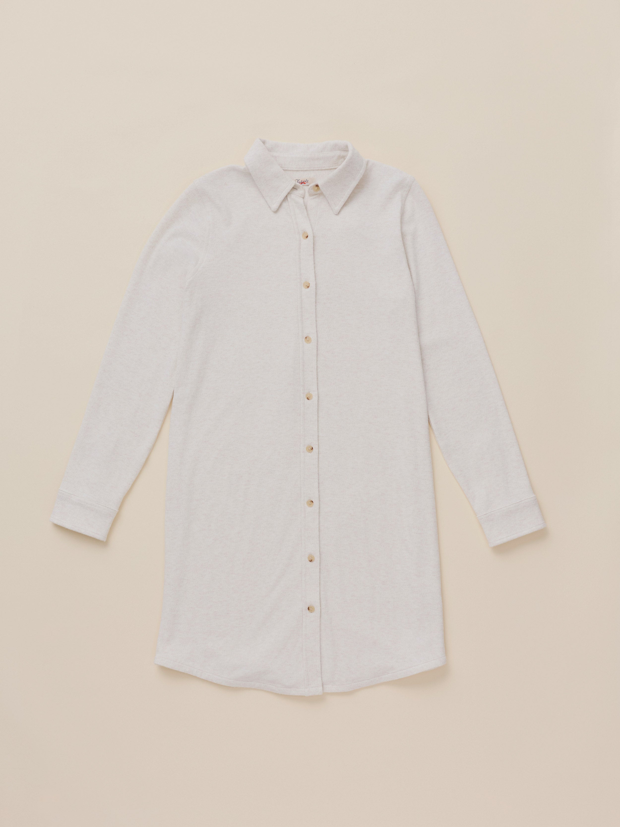 A light beige long-sleeve button-up shirt dress with a pointed collar, laid flat against a solid beige background.