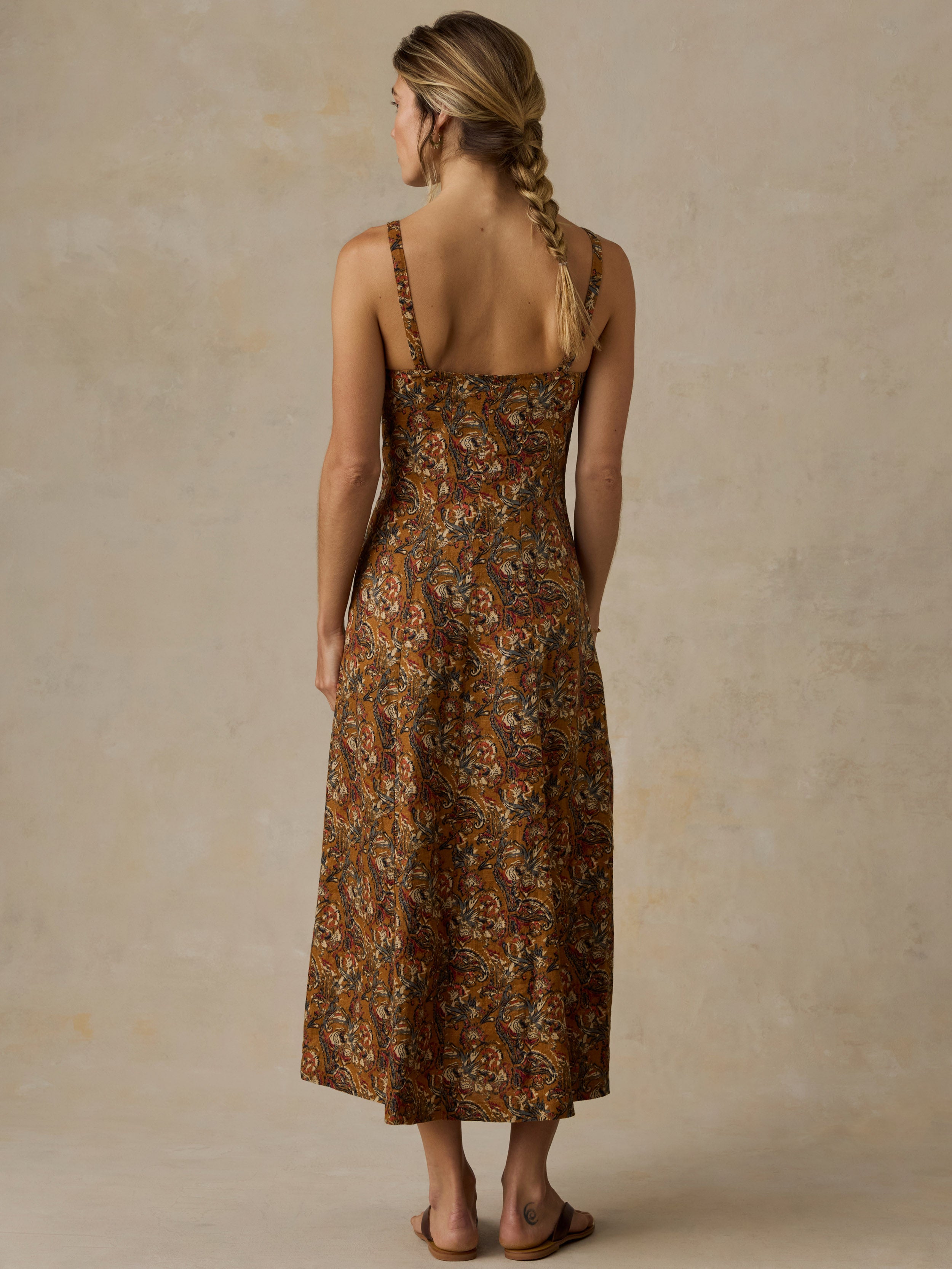 Woman wearing an orange and brown printed dress and sandals against a beige background