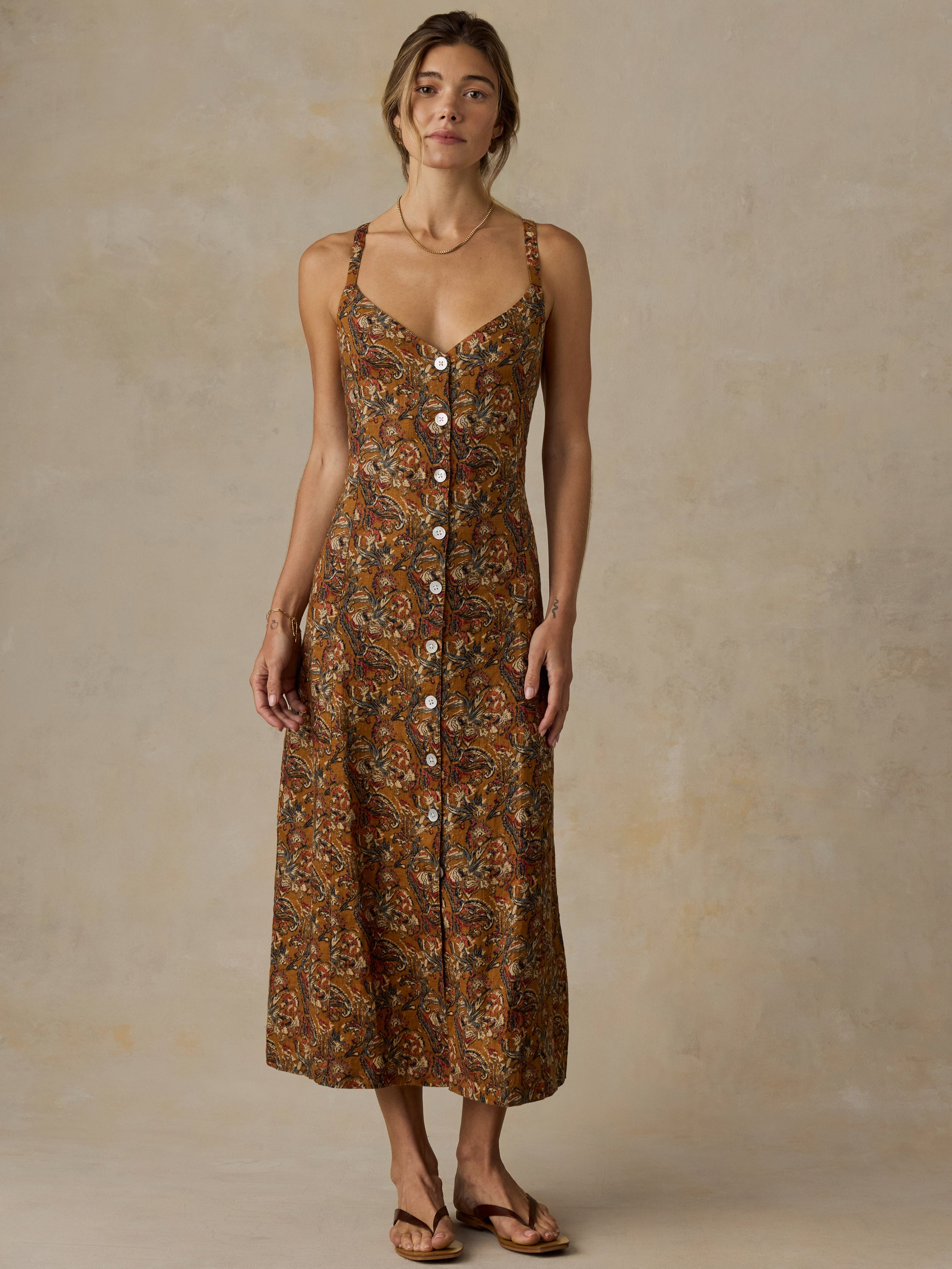 Woman wearing an orange and brown printed dress and sandals against a beige background